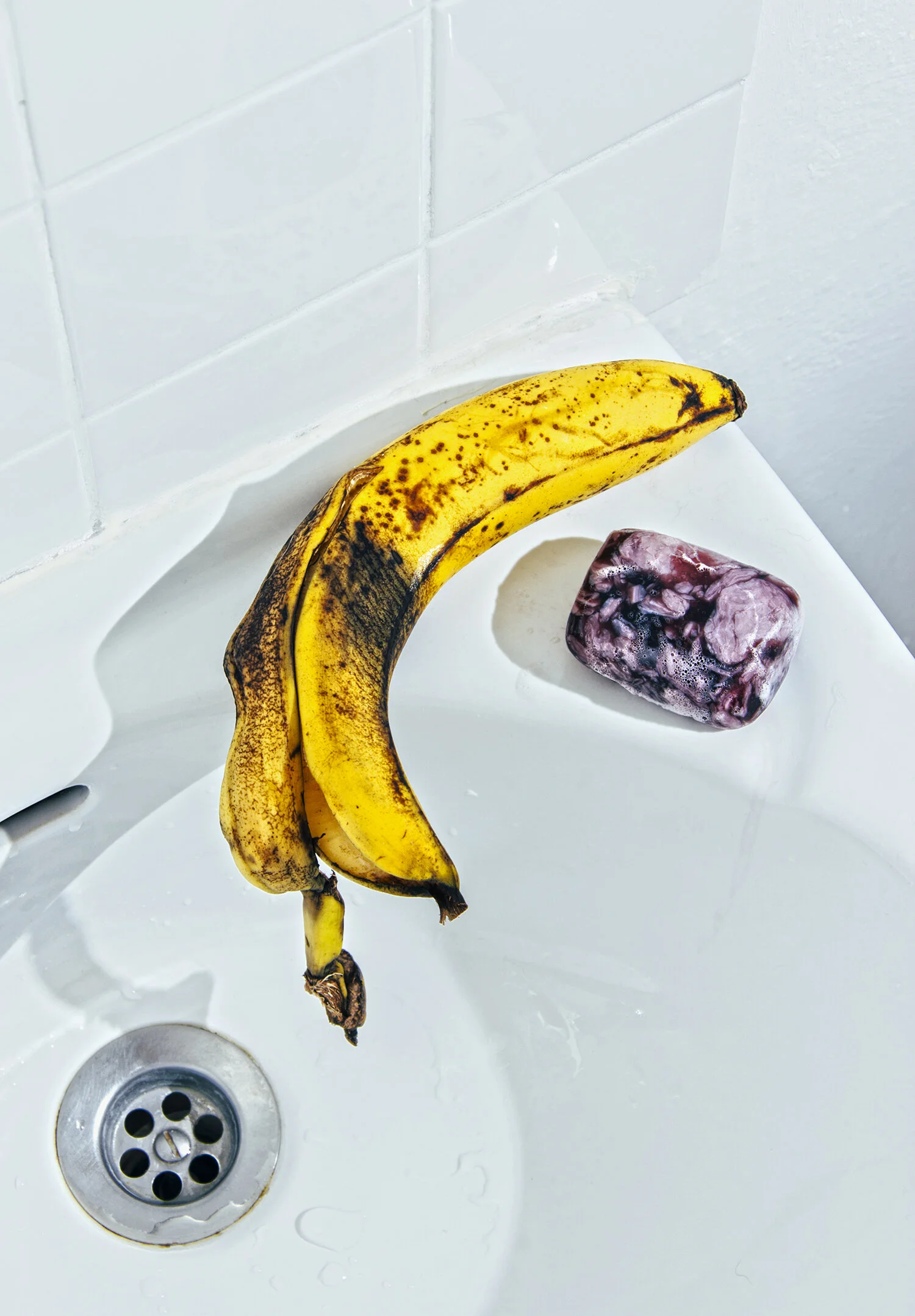 Dos plátanos maduros y una fruta blanca y morada en el lavabo blanco con tubo de desagüe