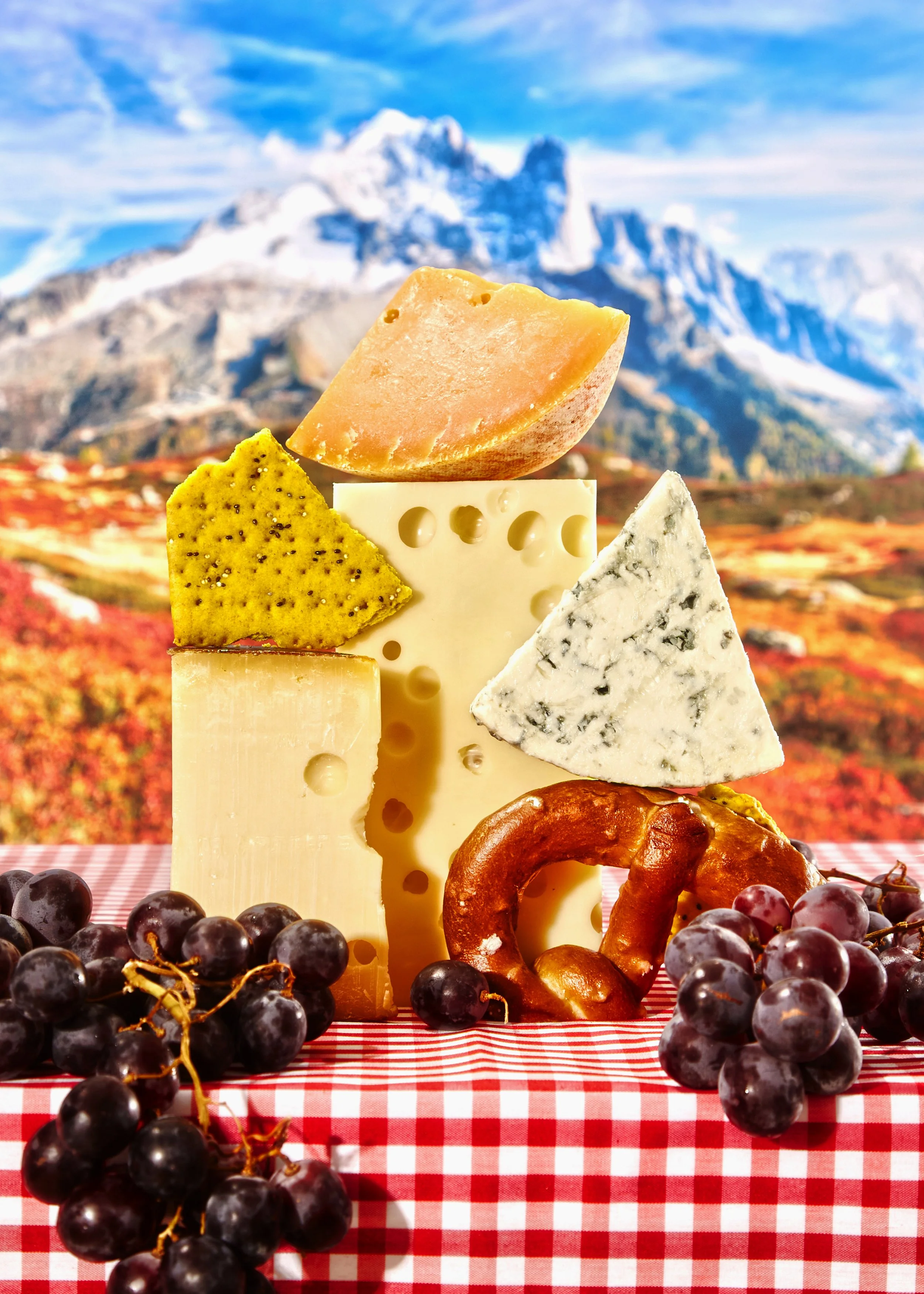 Queso, uvas, un pretzel, y una variedad de quesos en un fondo montañoso.