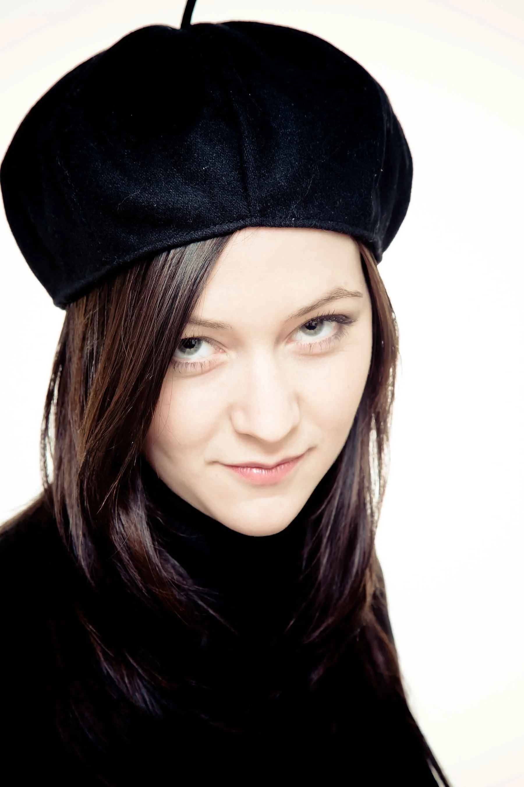 Jeune femme avec chapeau noir et vêtements noirs, regardant vers la caméra, fond blanc