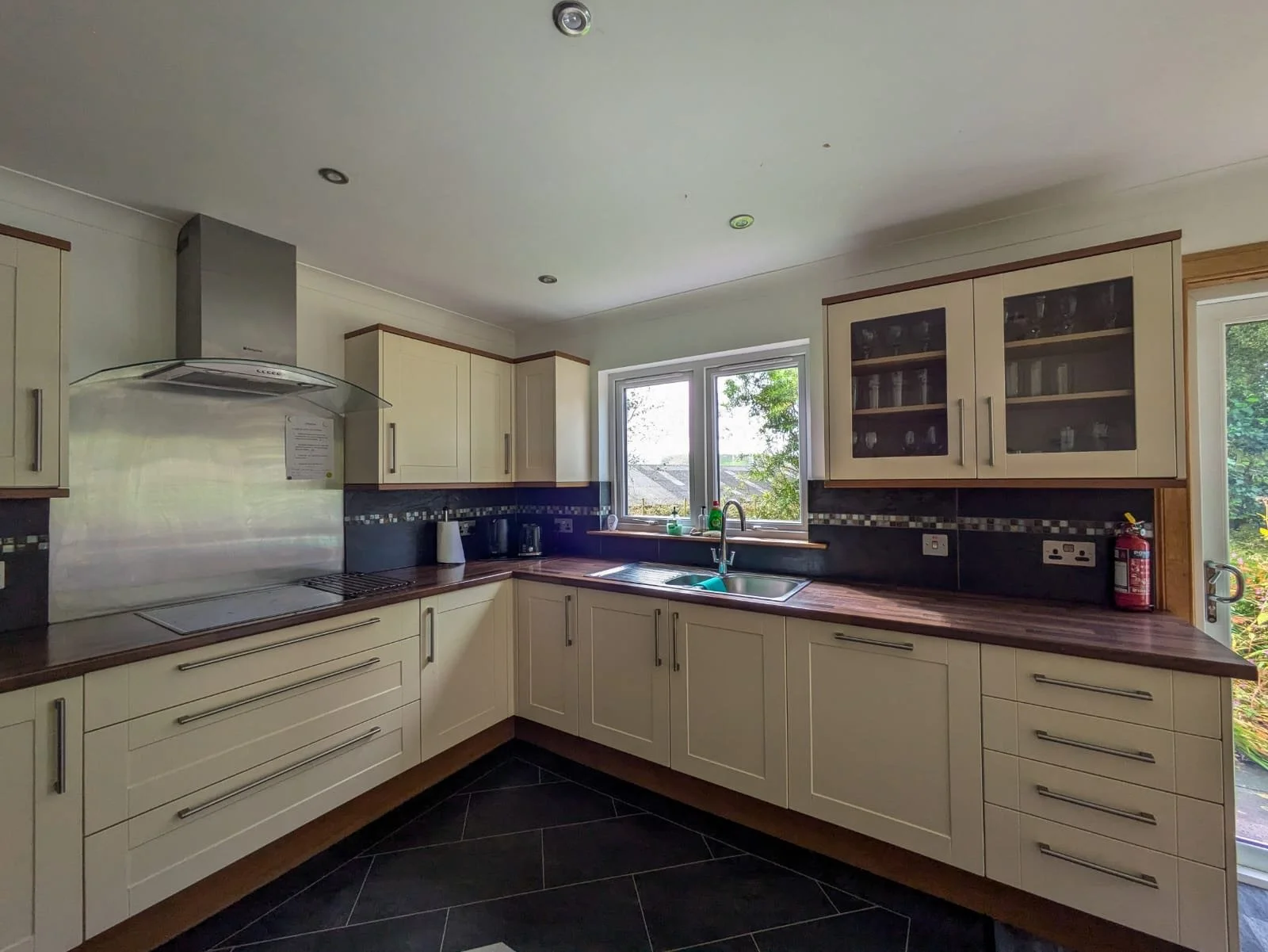 Modern kitchen with cream cabinets, dark countertops, and a window above the sink overlooking greenery.