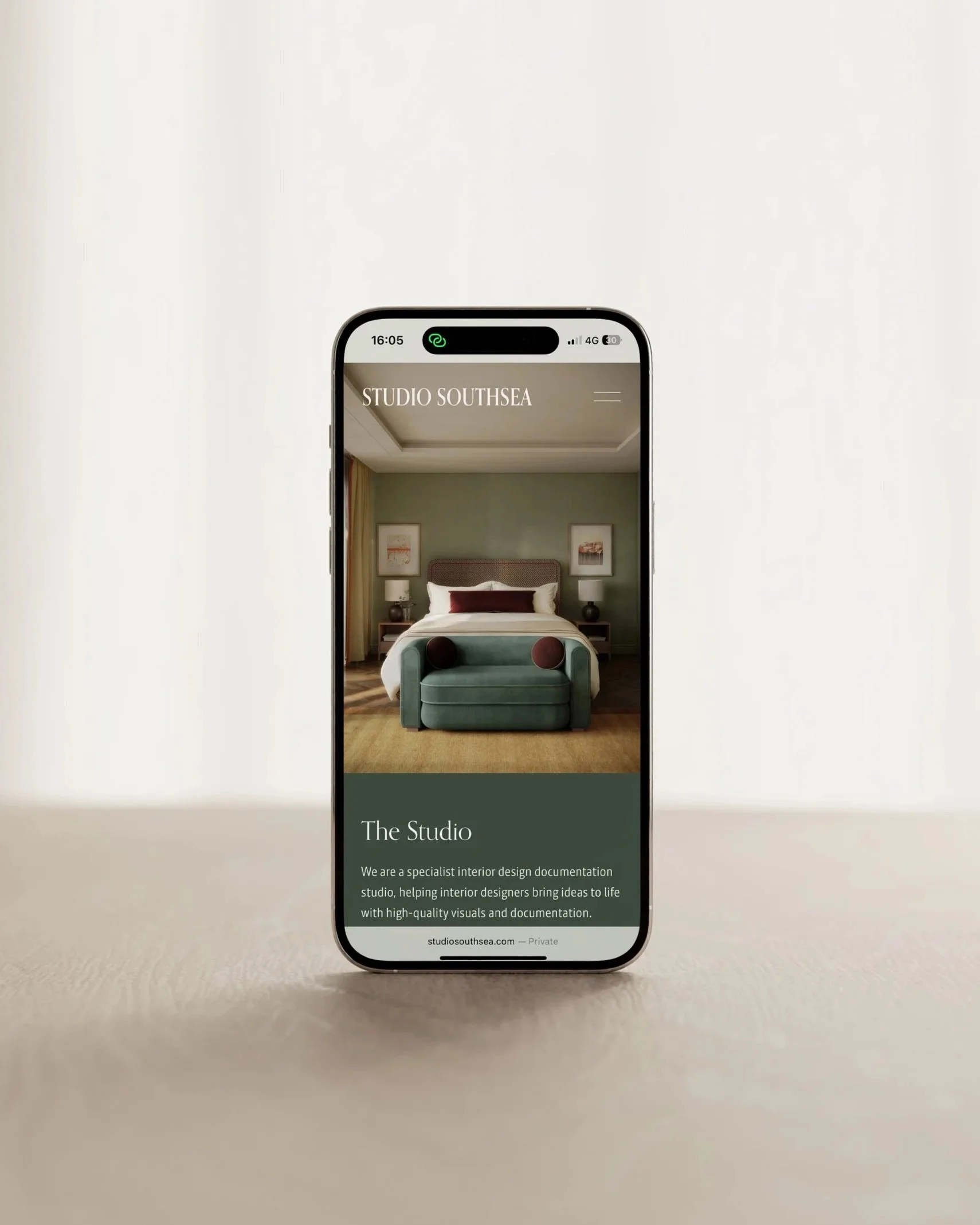 Smartphone displaying interior design studio website with a bedroom scene featuring a green sofa and artwork on the wall.
