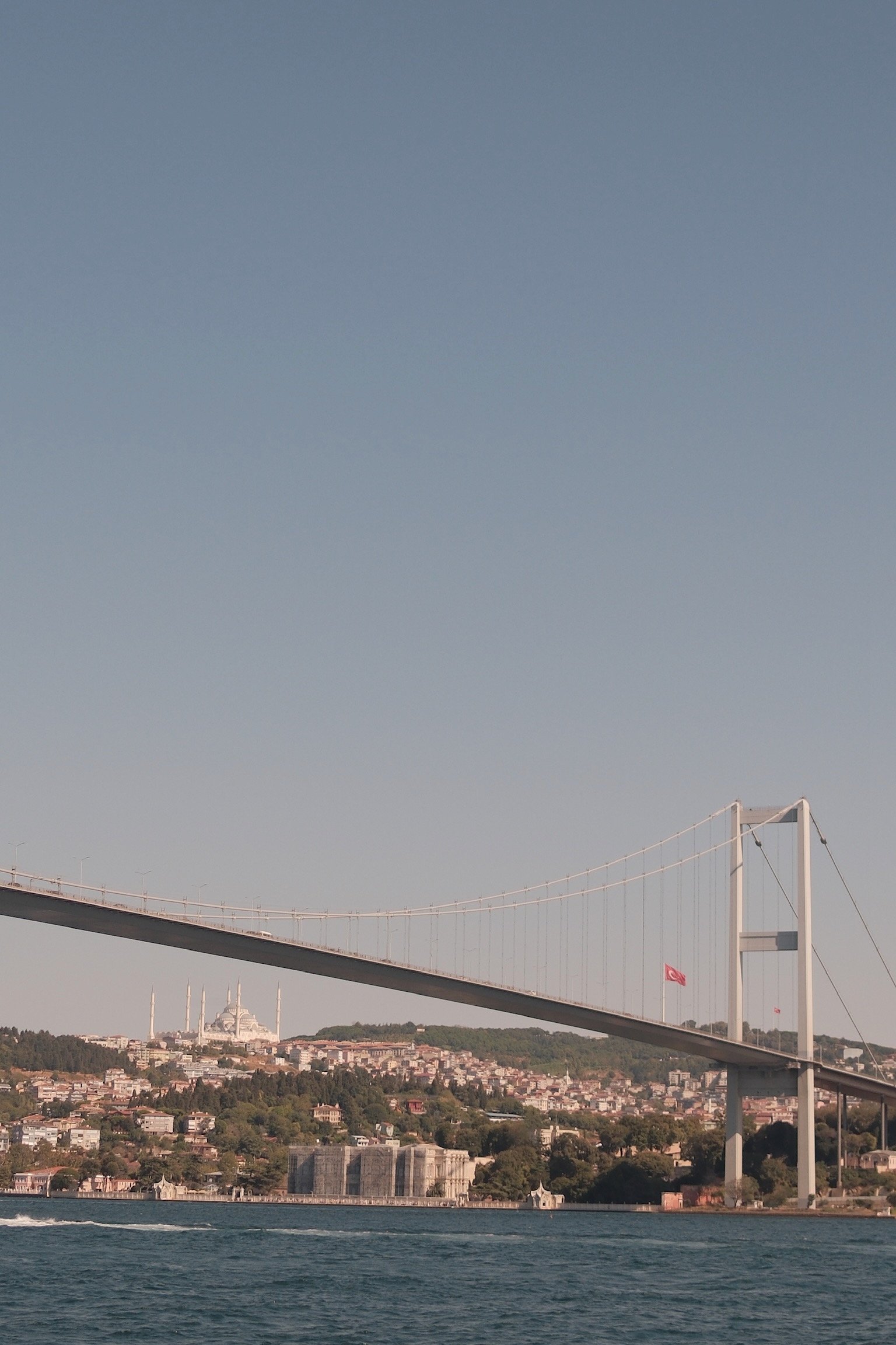 Blick auf den Bosporus mit einer großen Brücke und der Stadt Istanbul im Hintergrund, mit Moscheen und türkischer Flagge.