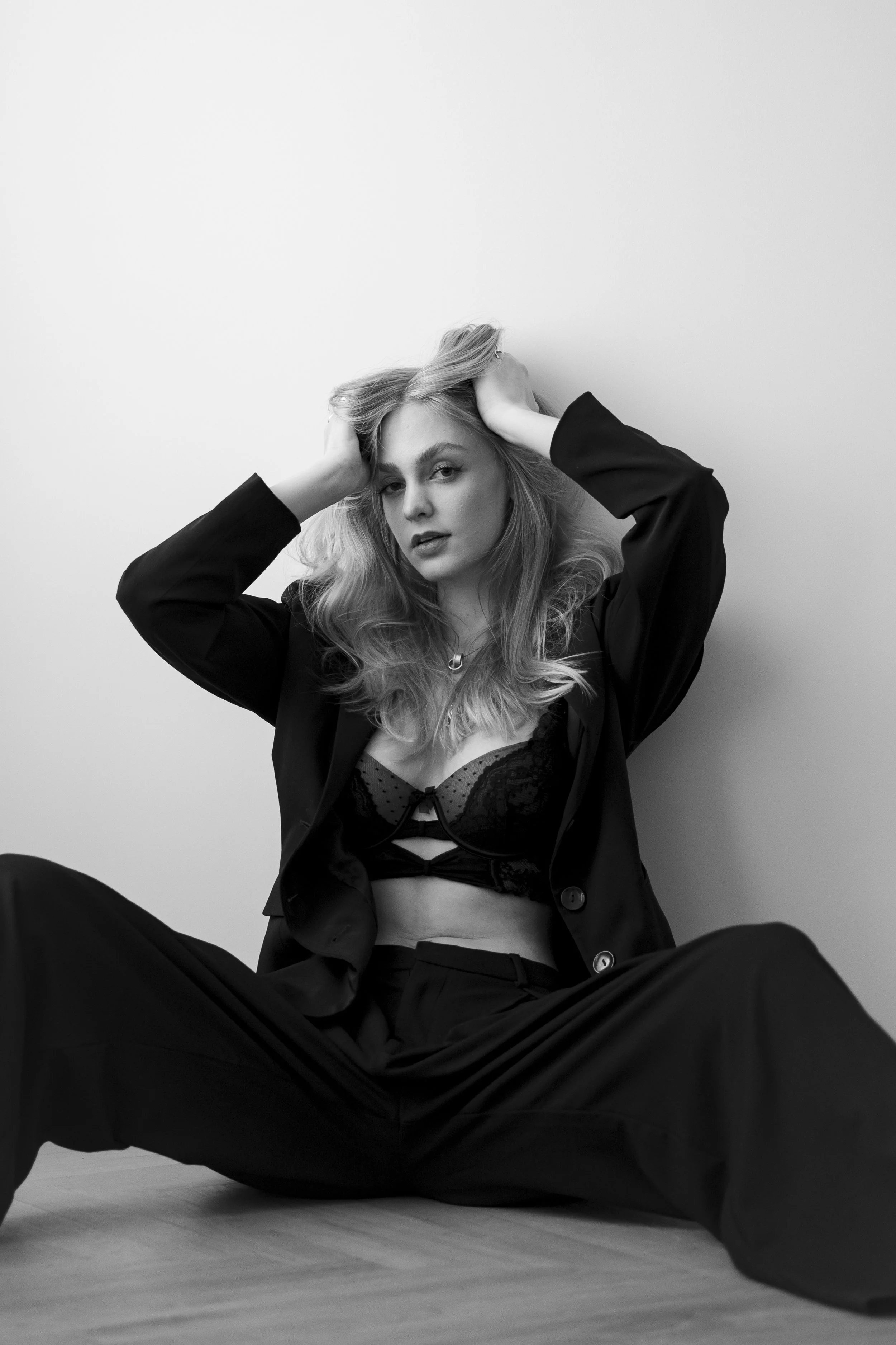 Schwarz-Weiß-Fotografie einer jungen Frau in Business-Hemd und BH, sitzend auf dem Boden, mit Haaren, die sie mit beiden Händen berührt.