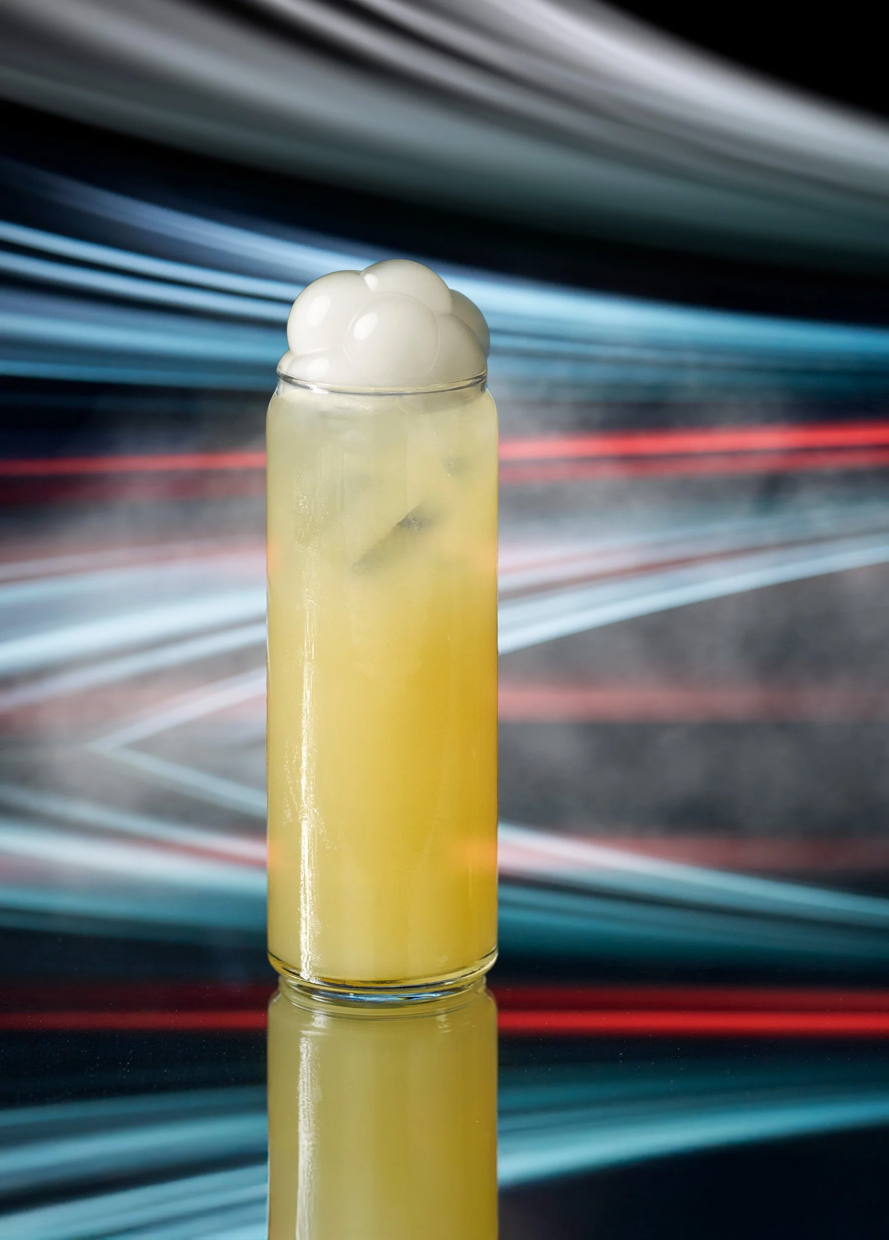 A tall glass of lemonade with ice cubes and a scoop of vanilla ice cream on top, against a blurred colorful light streak background.
