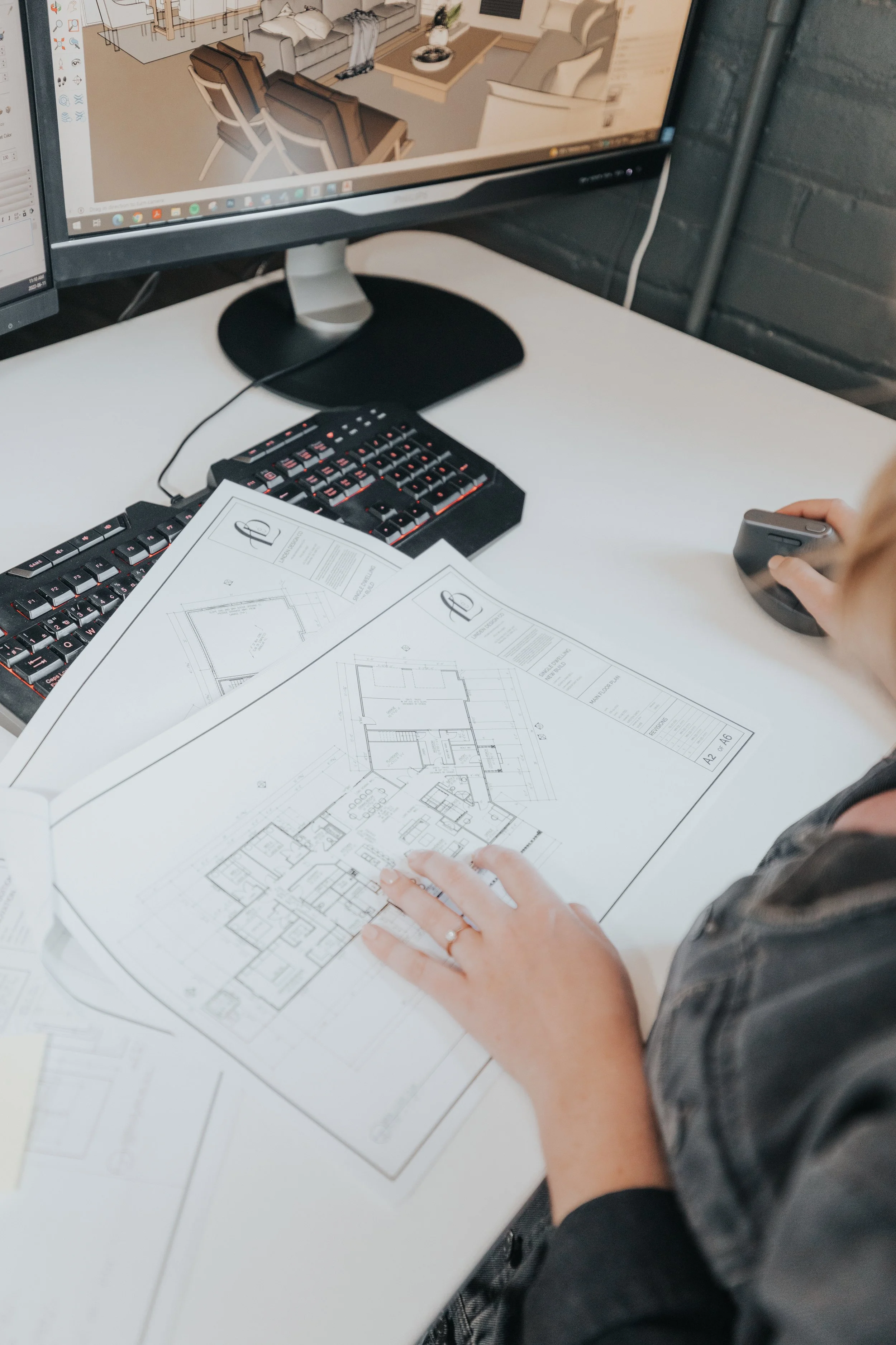 Person working on architectural blueprints at a desk with a computer and keyboard.
