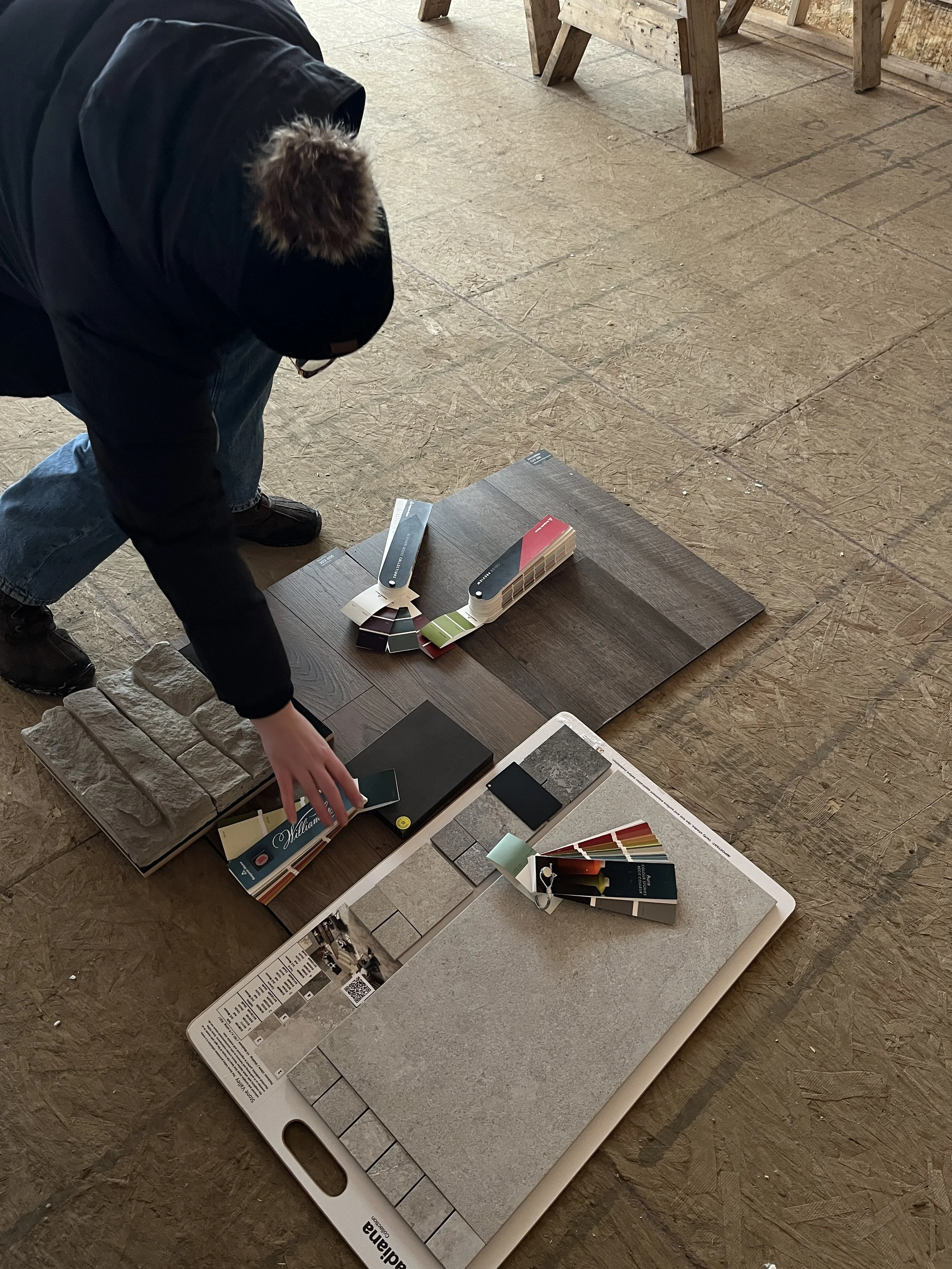 Person arranging paint and tile samples on the floor of a home improvement store or showroom.