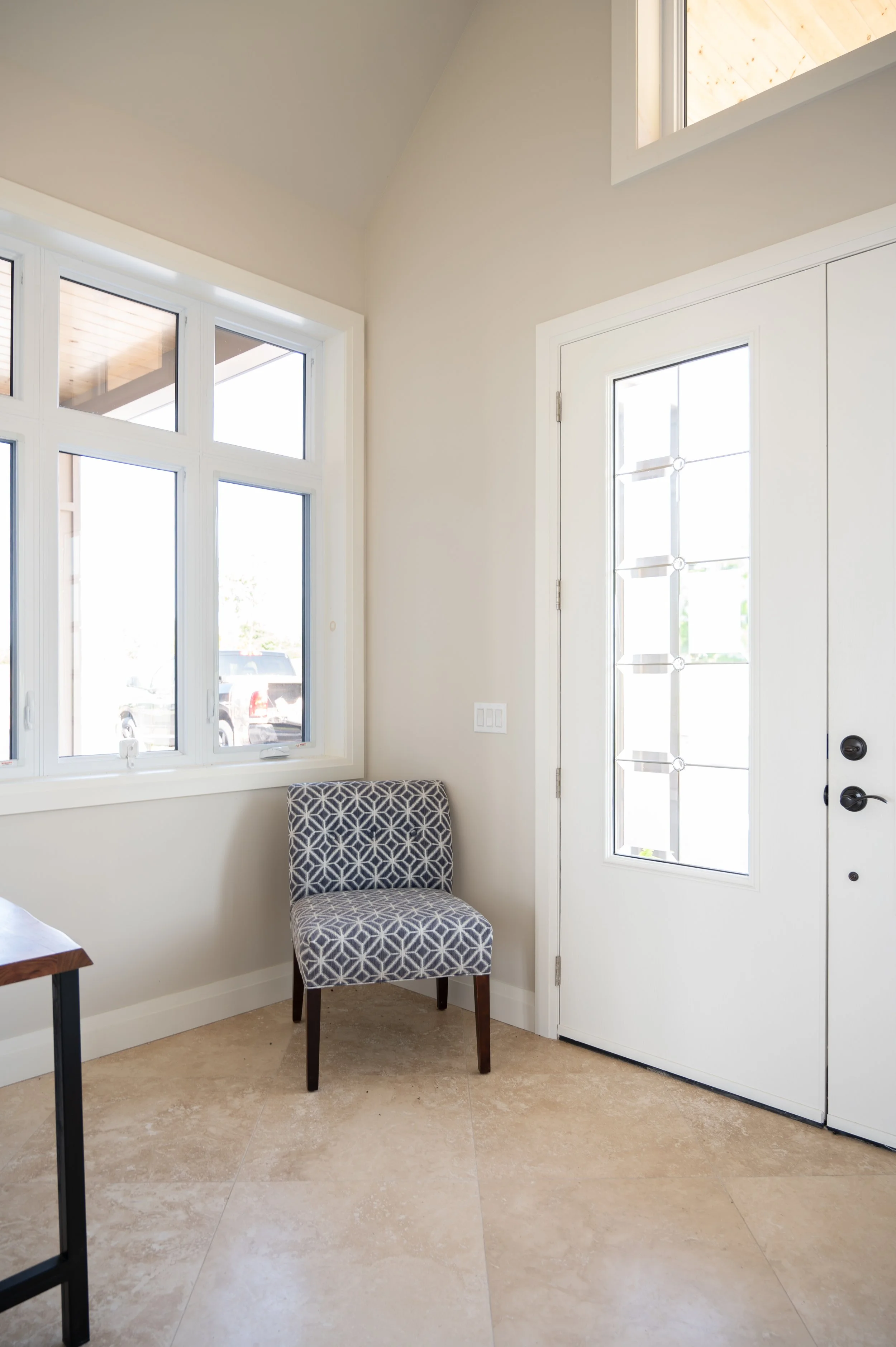 Interior view of a house entryway with a patterned chair, large windows, and a glass-paneled door.
