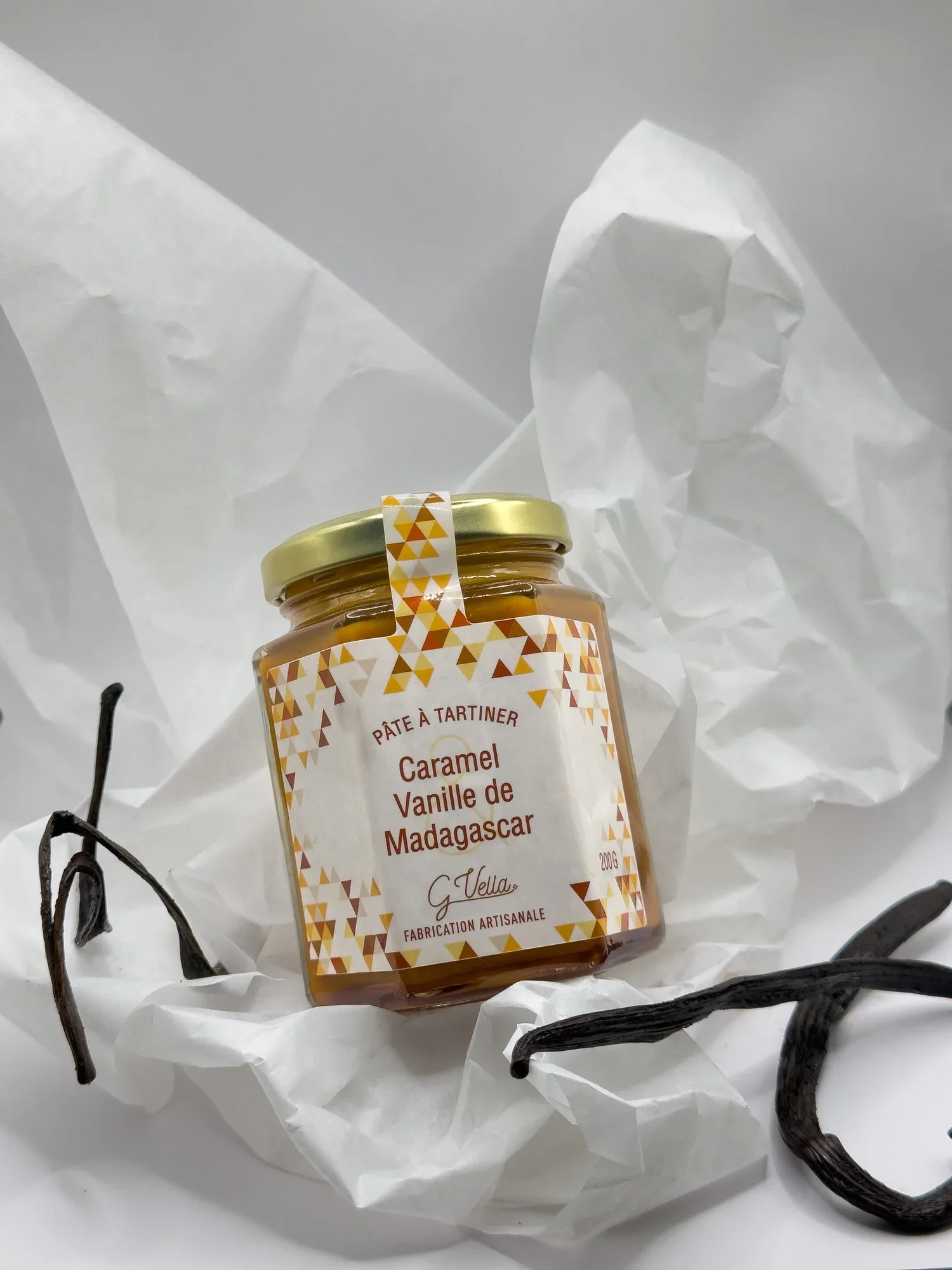 Pot de confiture de caramel vanille de Madagascar sur un lit de papier blanc, entouré de gousses de vanille droites et courbes
