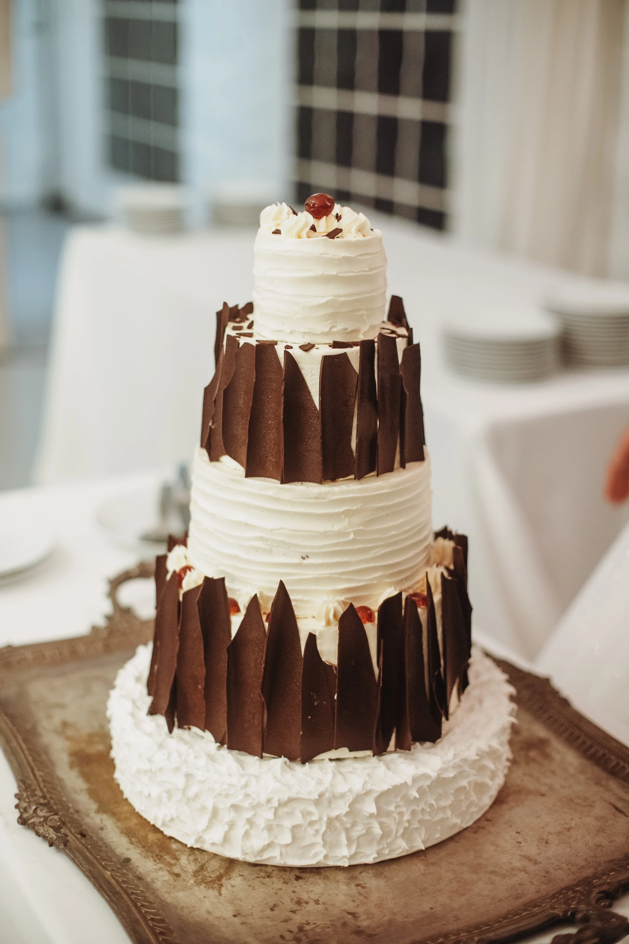 Gâteau à plusieurs niveaux décoré de chocolat noir et de crème, avec une petite décoration en haut et des couches de différentes textures.