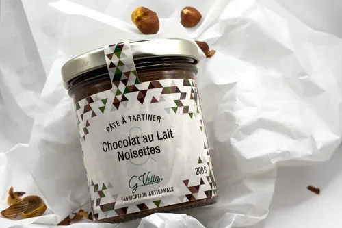 Pot de pâte à tartiner au chocolat au lait et noisettes avec quelques noisettes autour, sur du papier blanc