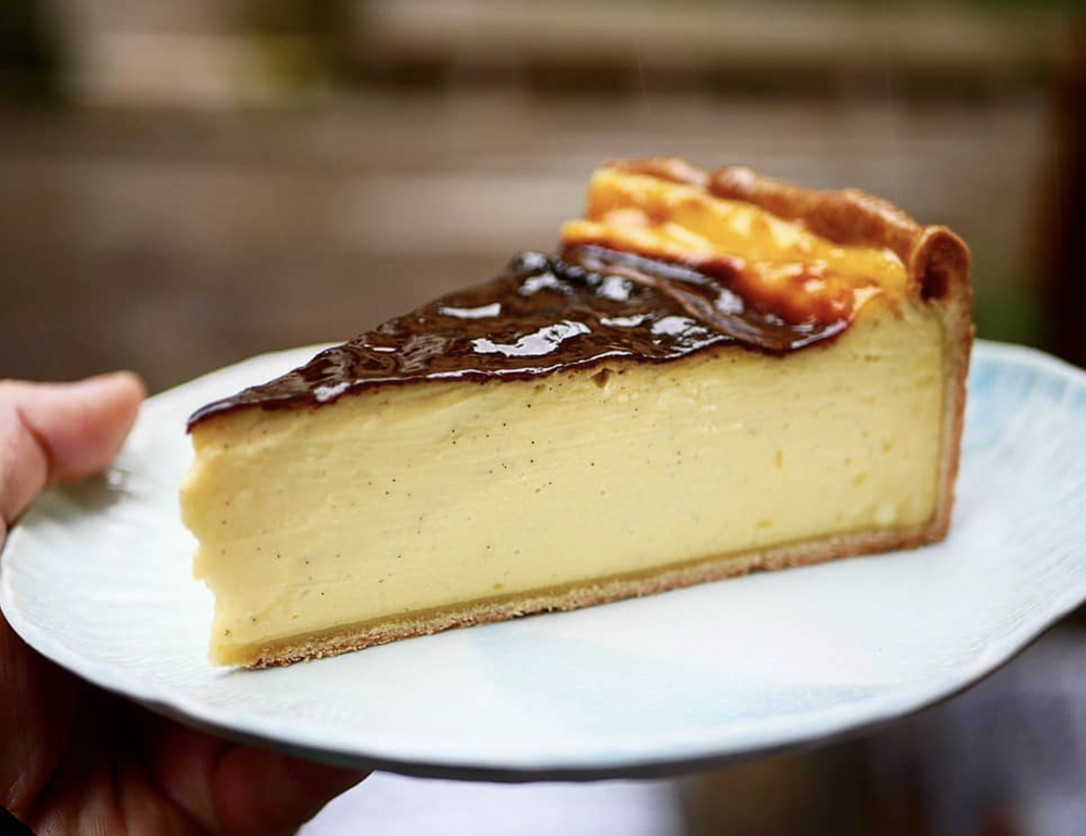 Part de tarte au fromage avec une croûte dorée et une surface de caramel, posée sur une assiette blanche.