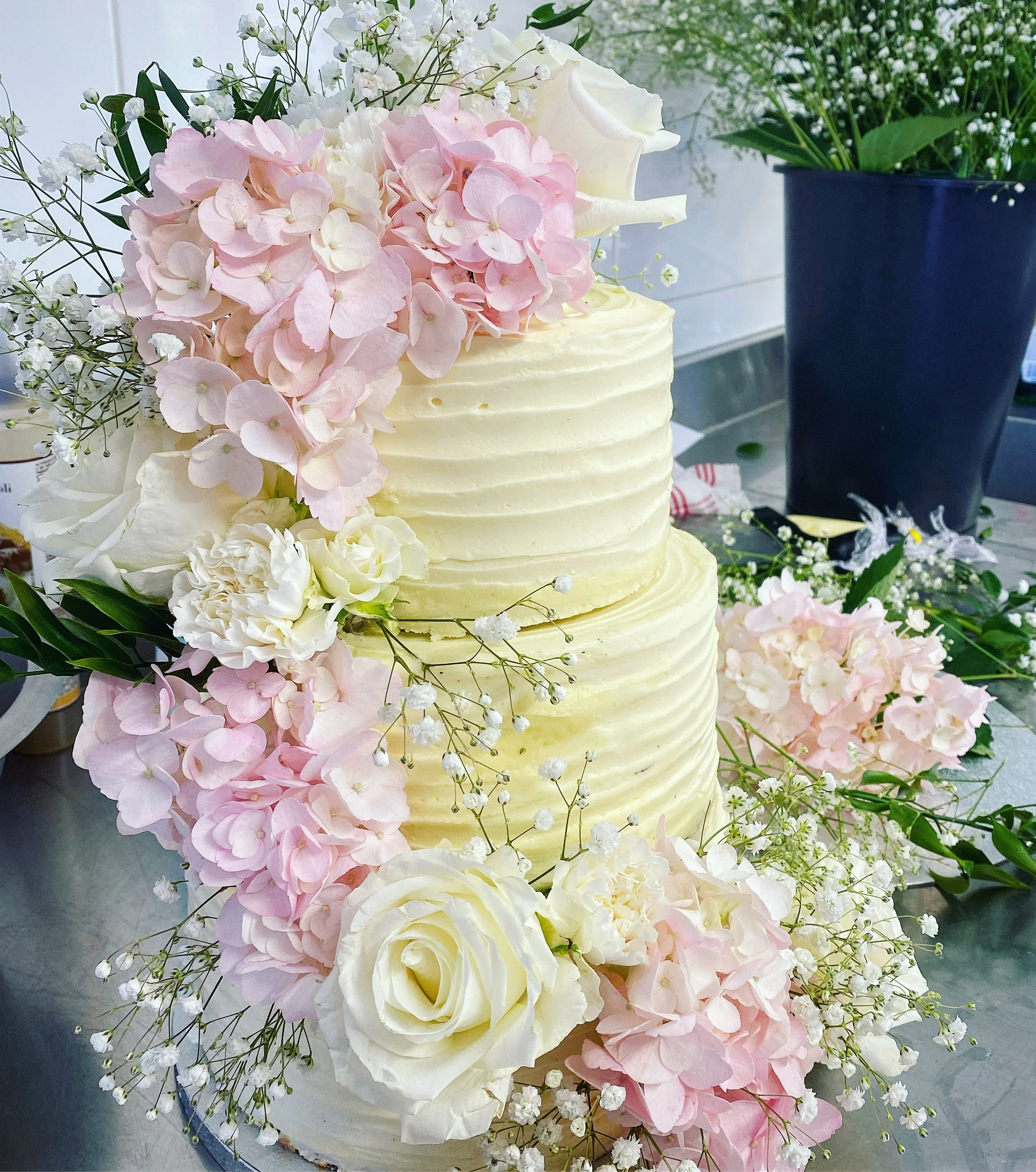 Gâteau de mariage à deux niveaux, décoré de fleurs blanches et roses, avec des hortensias, roses et petites fleurs blanches