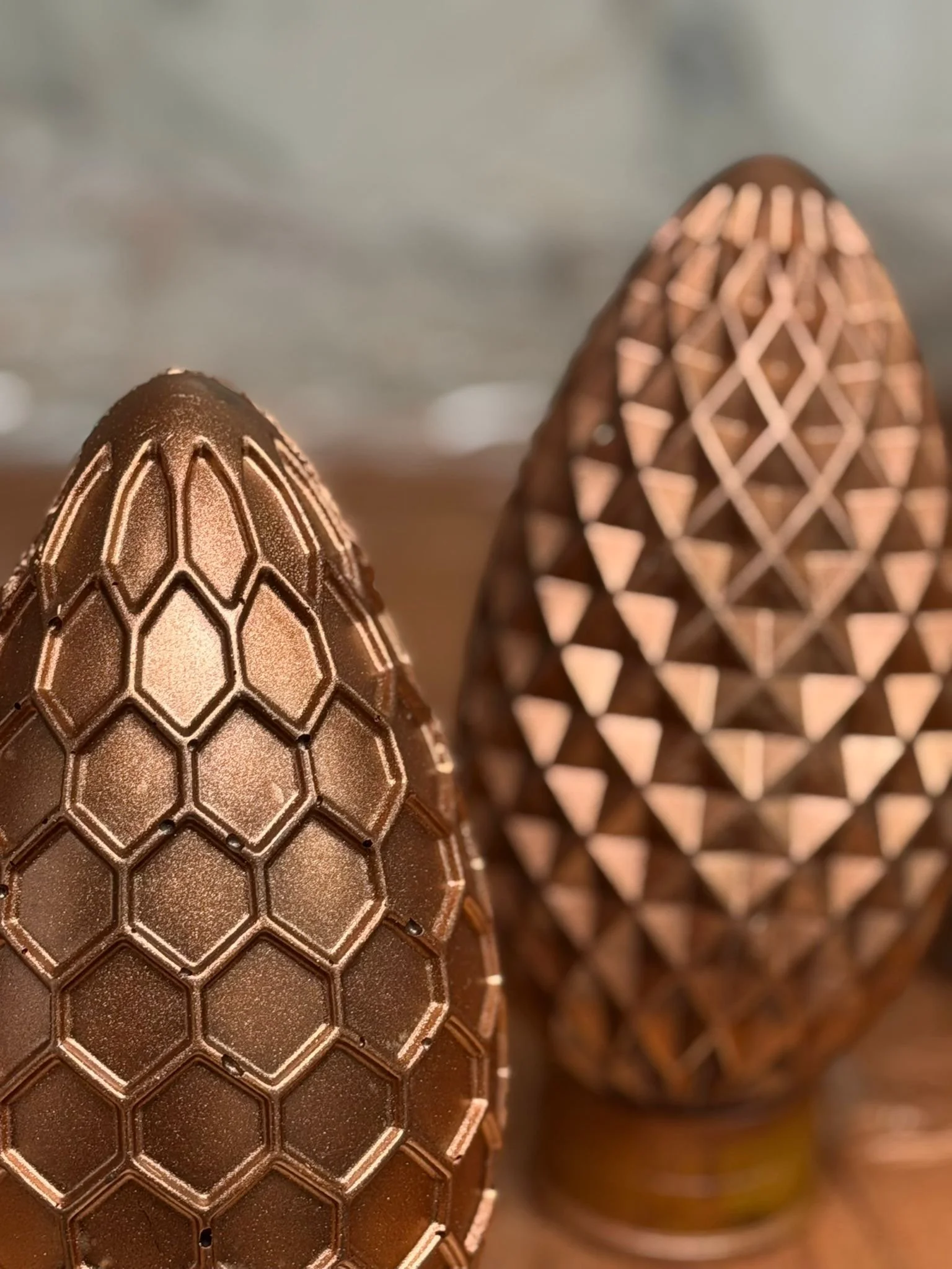 Deux œufs en chocolat avec des motifs géométriques en relief, l'un avec un motif en nid d'abeille et l'autre avec un motif en triangles.