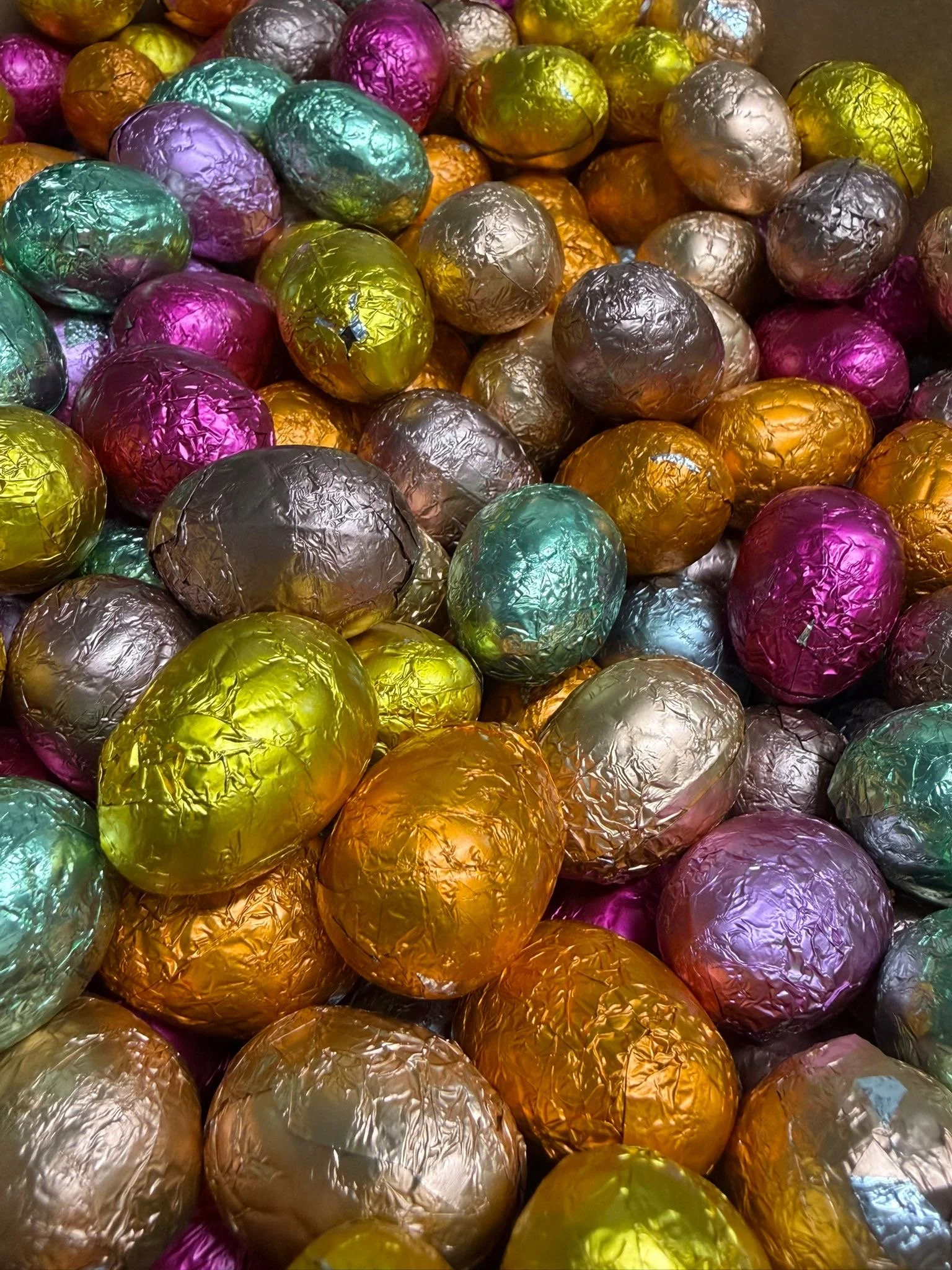 Œufs en chocolat colorés enveloppés de papier d'aluminium de différentes couleurs, superposés et empilés.