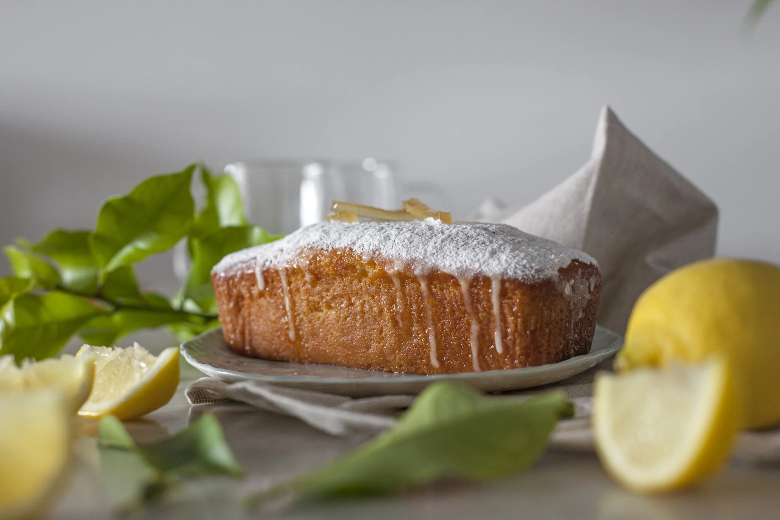 Gâteau au citron avec glaçage blanc, citron coupé, feuilles vertes, et serviette beige sur une table.