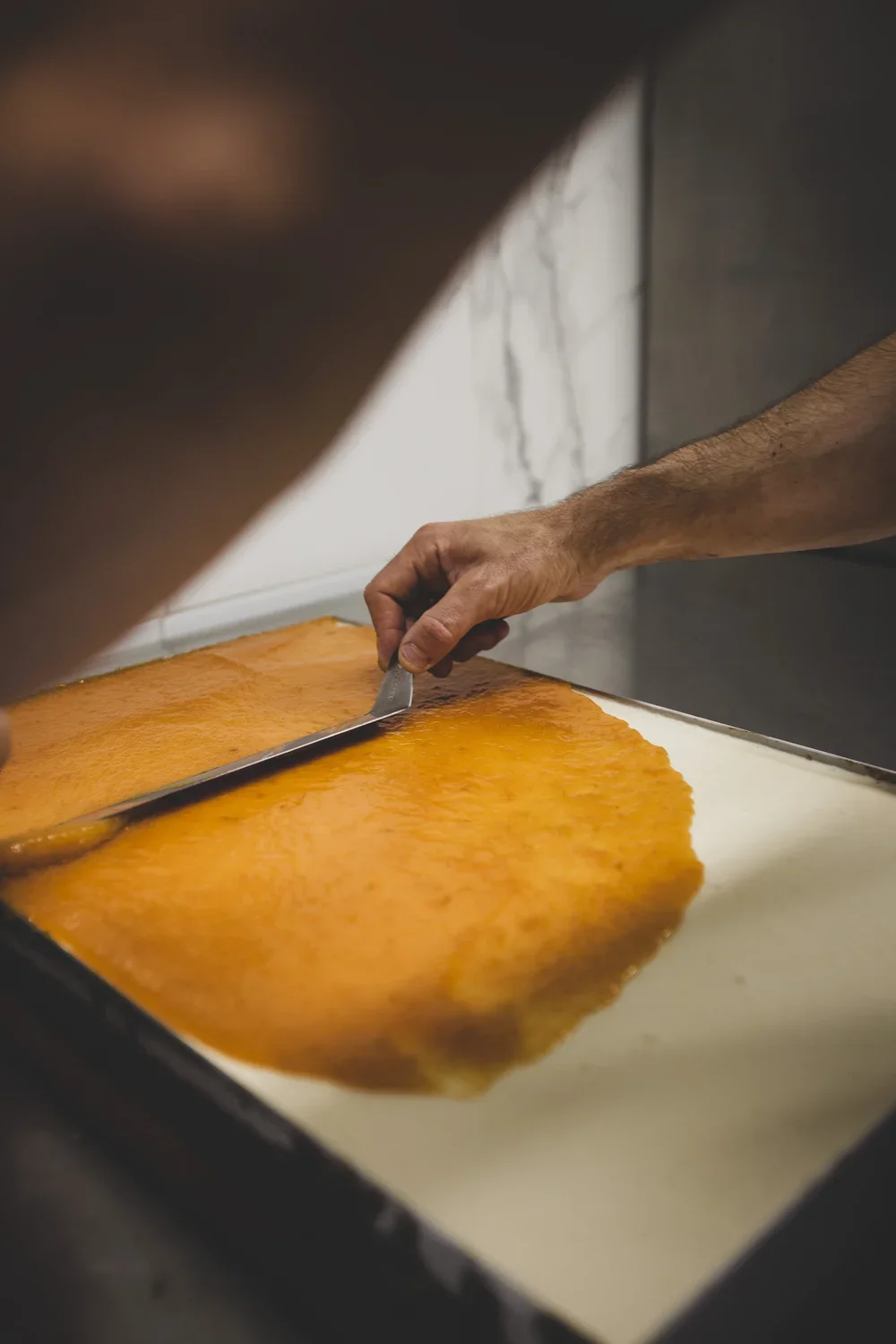 Une personne coupe une plaque de caramel dur sur une surface rectangulaire.