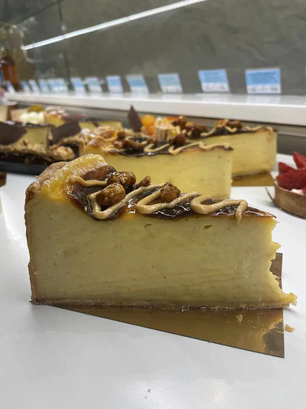 Gâteau au fromage décoré avec des noix, du chocolat et du glaçage au caramel, présenté en tranches.