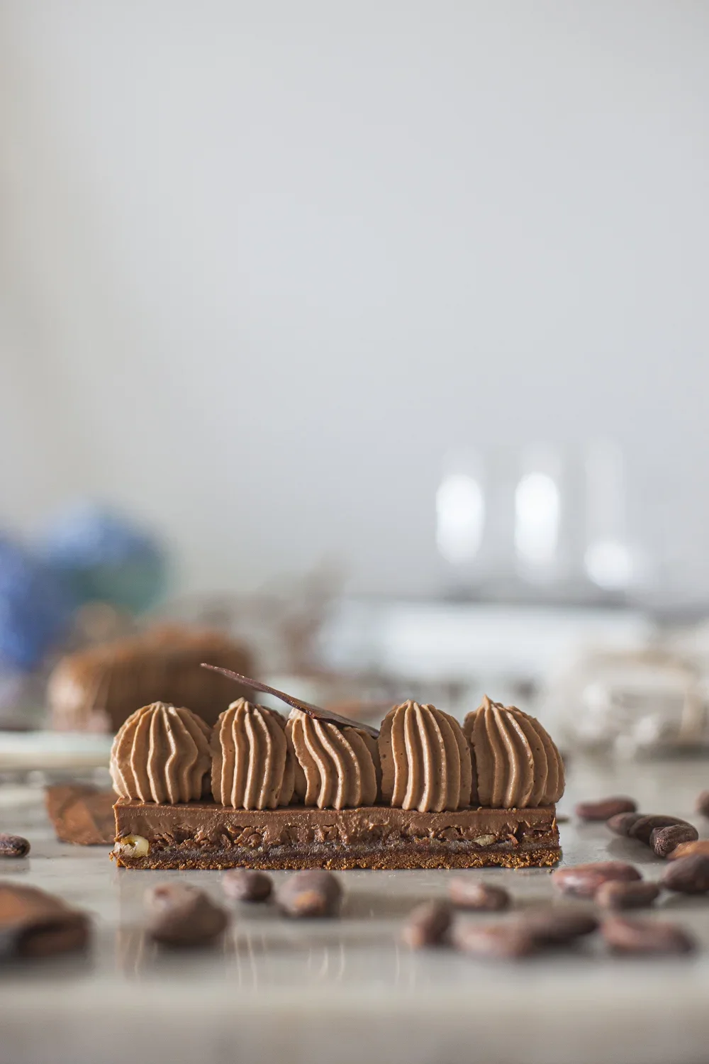 Une tarte au chocolat décorée de doris de crème au chocolat, entourée de fèves de cacao sur une surface en marbre.