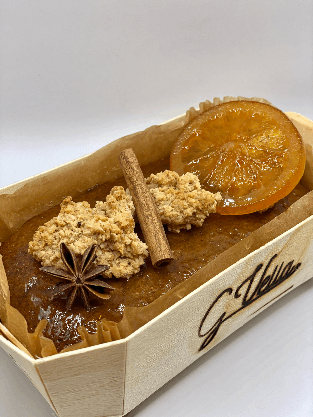 Gâteau décoré avec des tranches d'orange, de la cannelle, du crumble et des pasta dans une boîte en bois.