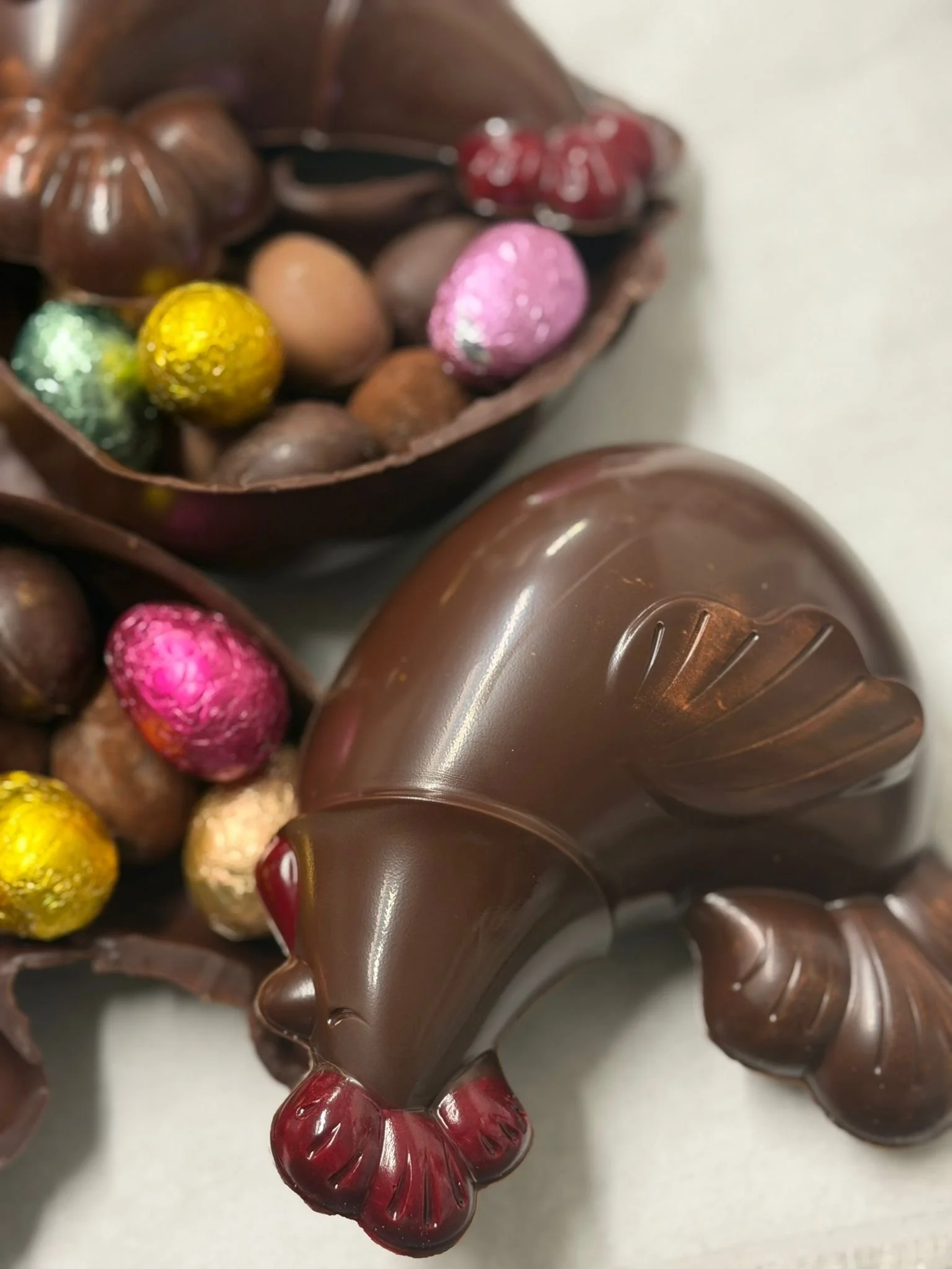 Œuf en chocolat en forme de poule avec des petits œufs en chocolat colorés et décorés, en partie dans une coquille en chocolat
