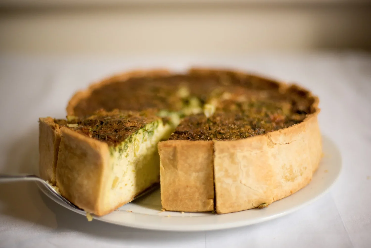 Tarte salée avec une croûte dorée et une garniture aux épinards et fromage, une portion est coupée