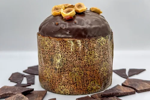 Un gâteau rond recouvert de glaçage au chocolat avec des noix en haut, entouré de morceaux de chocolat sur une surface blanche.