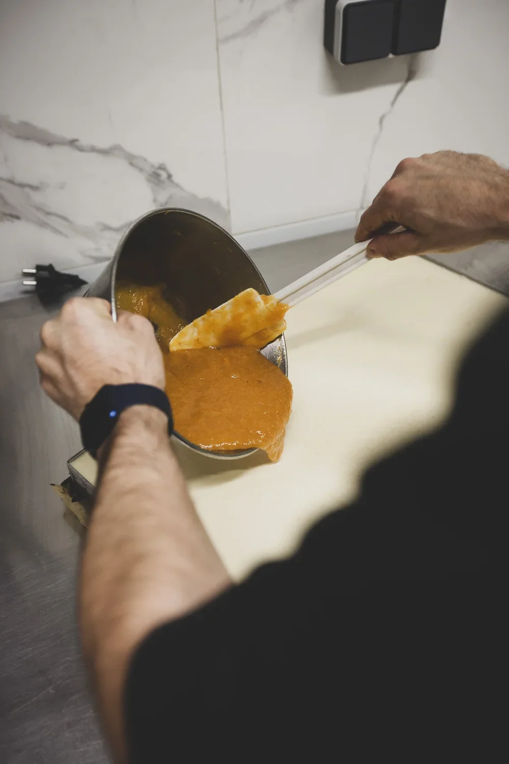 Une personne verse de la sauce dans un bol en métal, utilisant des baguettes, dans une cuisine moderne.