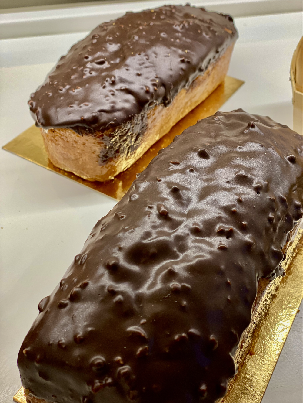 Deux bûches glacées au chocolat avec une couche de chocolat brillant sur le dessus, posées sur une surface dorée.