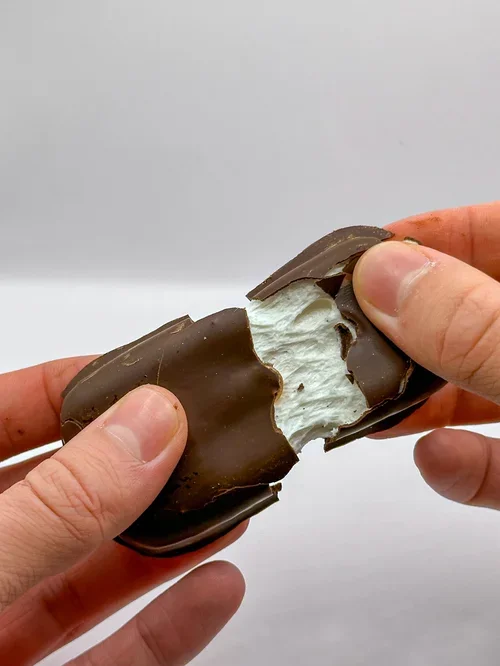Les mains tenant un bar de chocolat avec une garniture blanche, partiellement mangé.