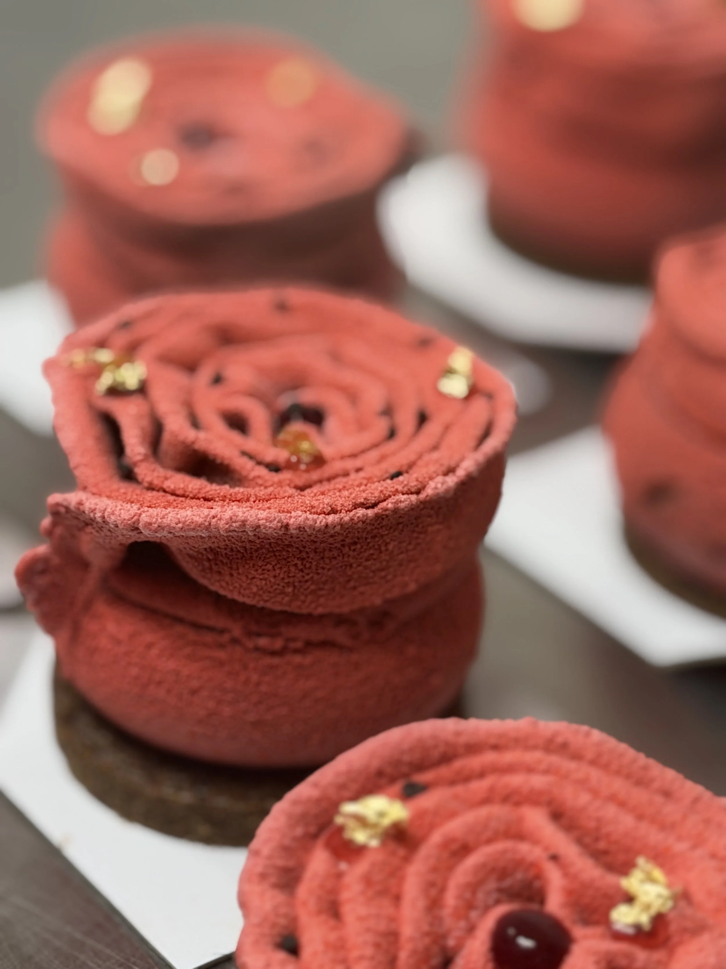 gâteaux en forme de roses rouges décorés de petites fleurs dorées, présentés sur des plateaux