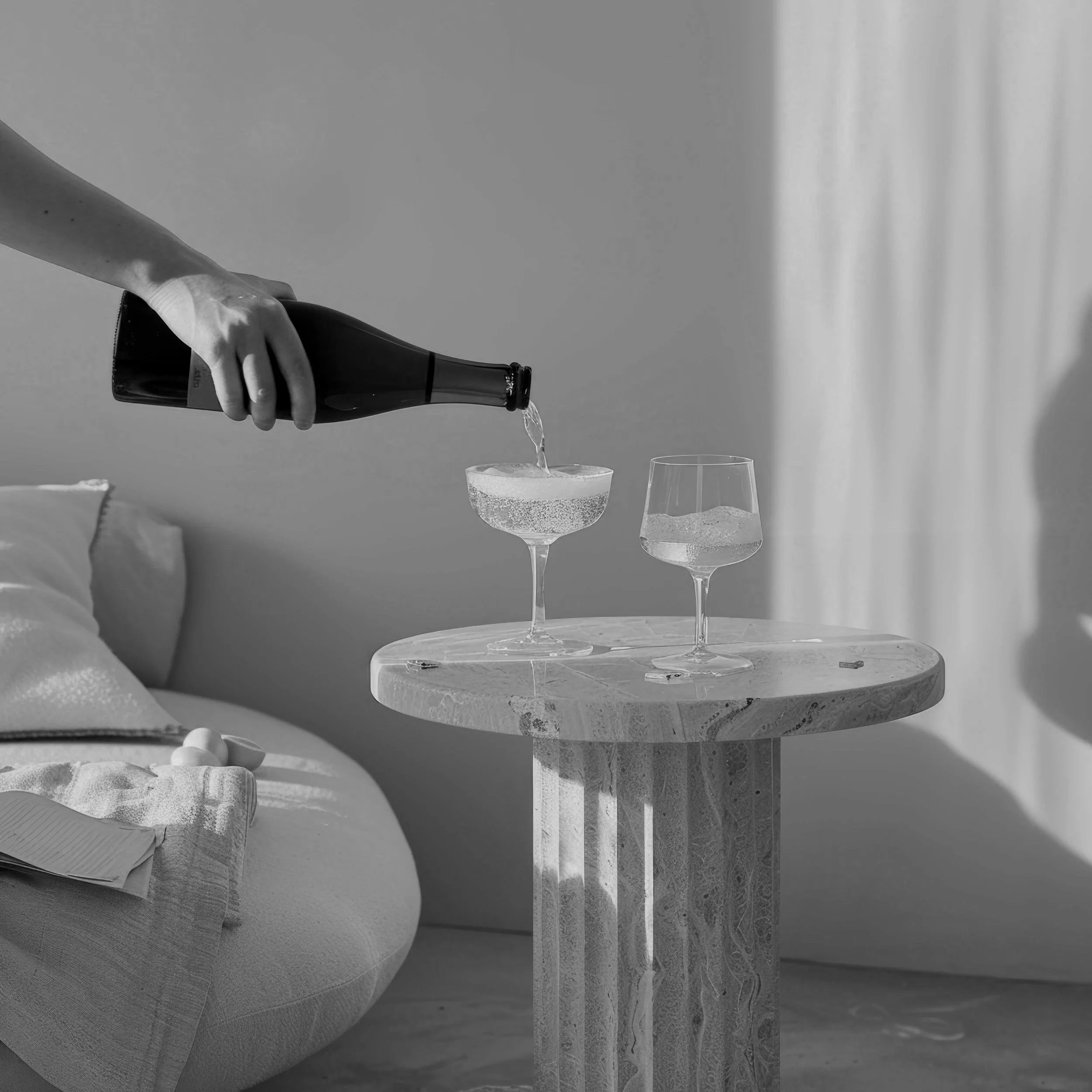 A woman with long blonde hair working on a silver laptop in a cream-colored suit on a cream couch.