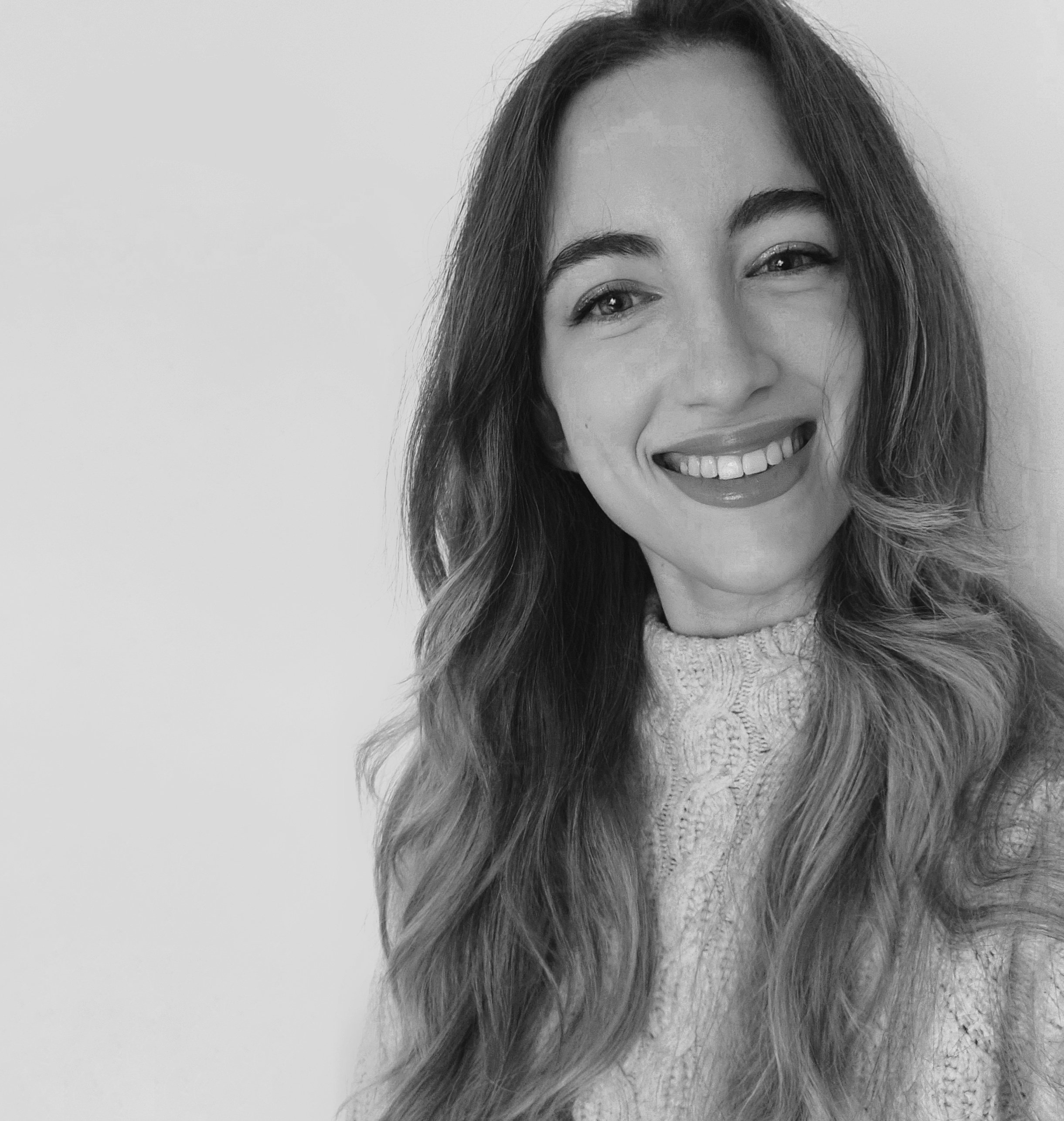 Black and white portrait of a smiling woman with long wavy hair, wearing a knitted sweater.