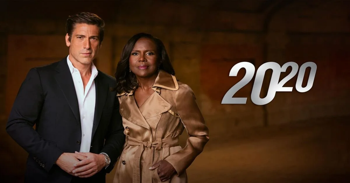 A man in a black suit and a woman in a tan trench coat stand side by side against a dark wooden background, with the year "2020" in gray text to their right.