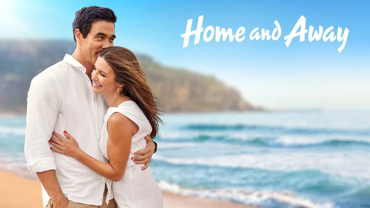A smiling couple embracing on a beach, with the words "Home and Away" in the sky above them.