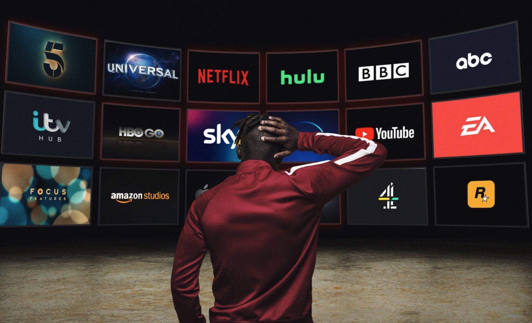 A person in a red jacket standing with their hand on their head, facing a wall of television screens displaying various streaming service logos like Netflix, Hulu, Disney+, YouTube, and others.