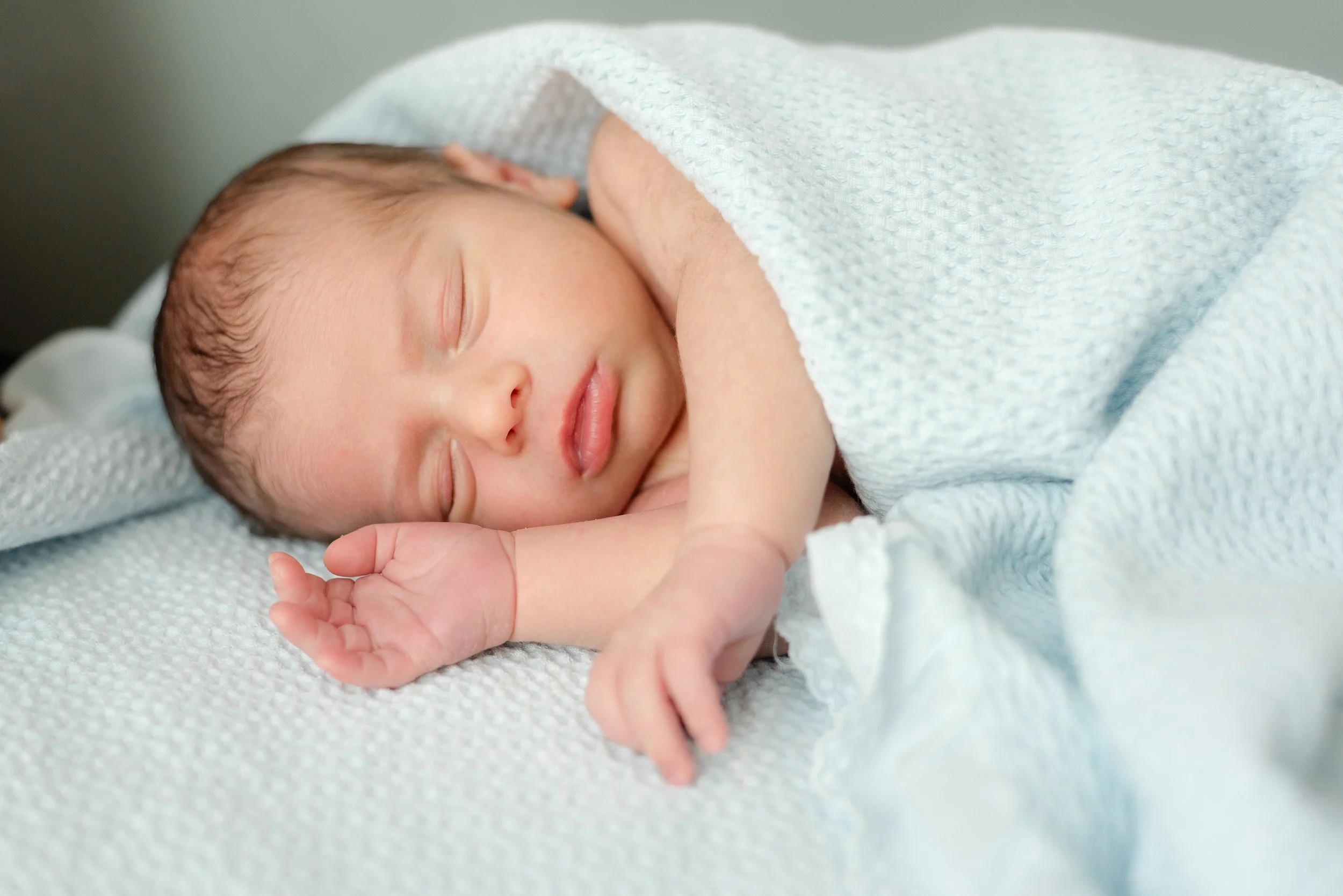 Close-up of a sleeping newborn baby wrapped in a white blanket.