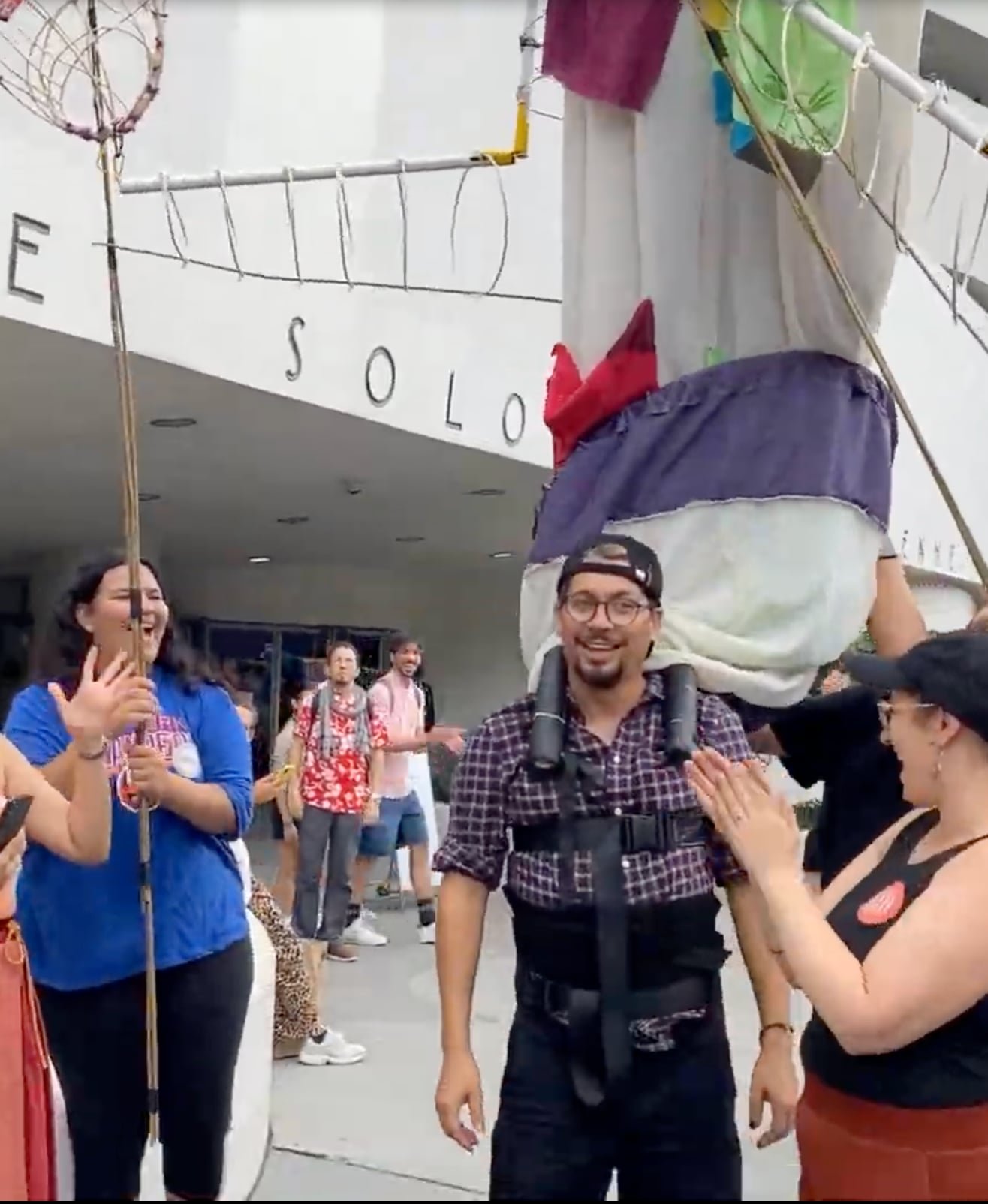 Oscar smiling while wearing a giant puppet as teens look on outside the Guggenheim Museum.