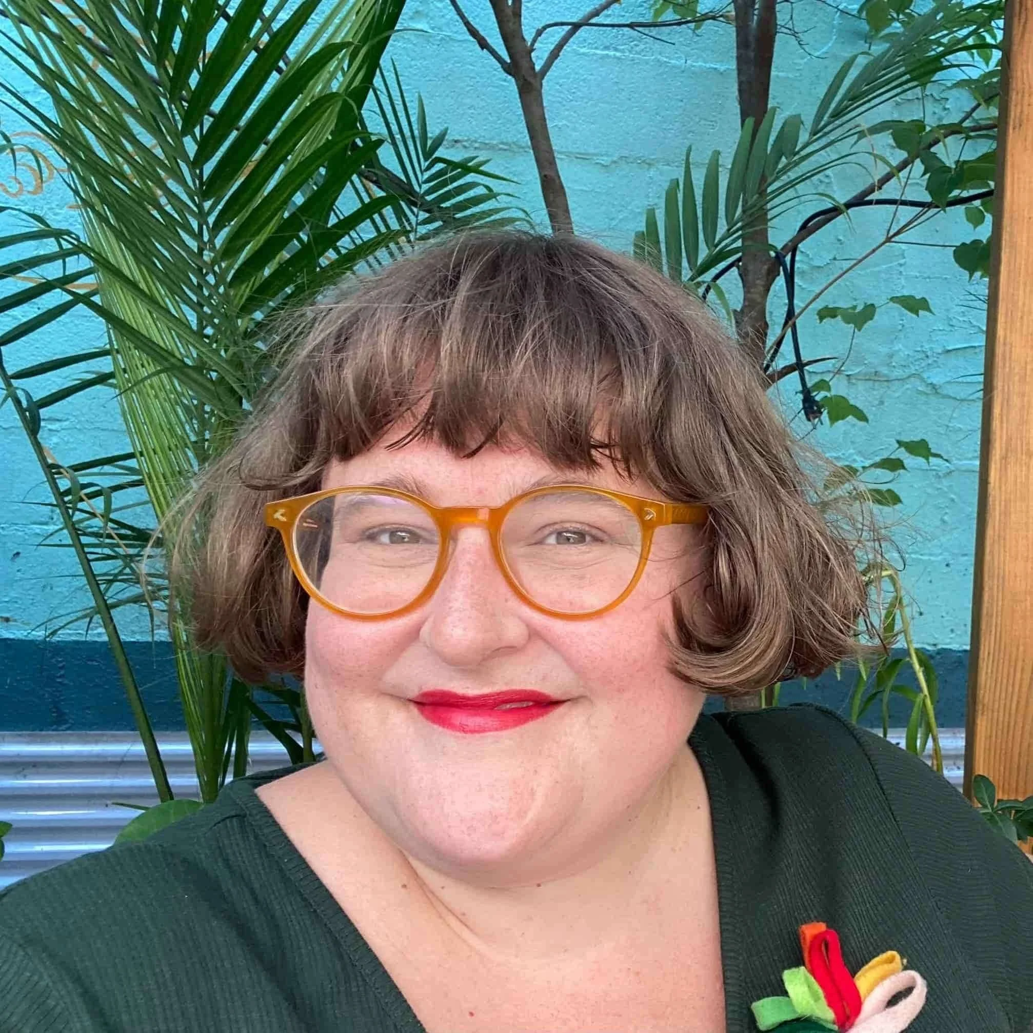 Headshot of susanna Brock, wearing orange glasses and a green shirt