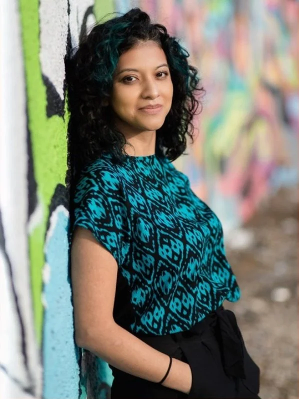 Professional photo of Daniela Kriedler leaning against a wall with graffiti on it in a blue patterned top