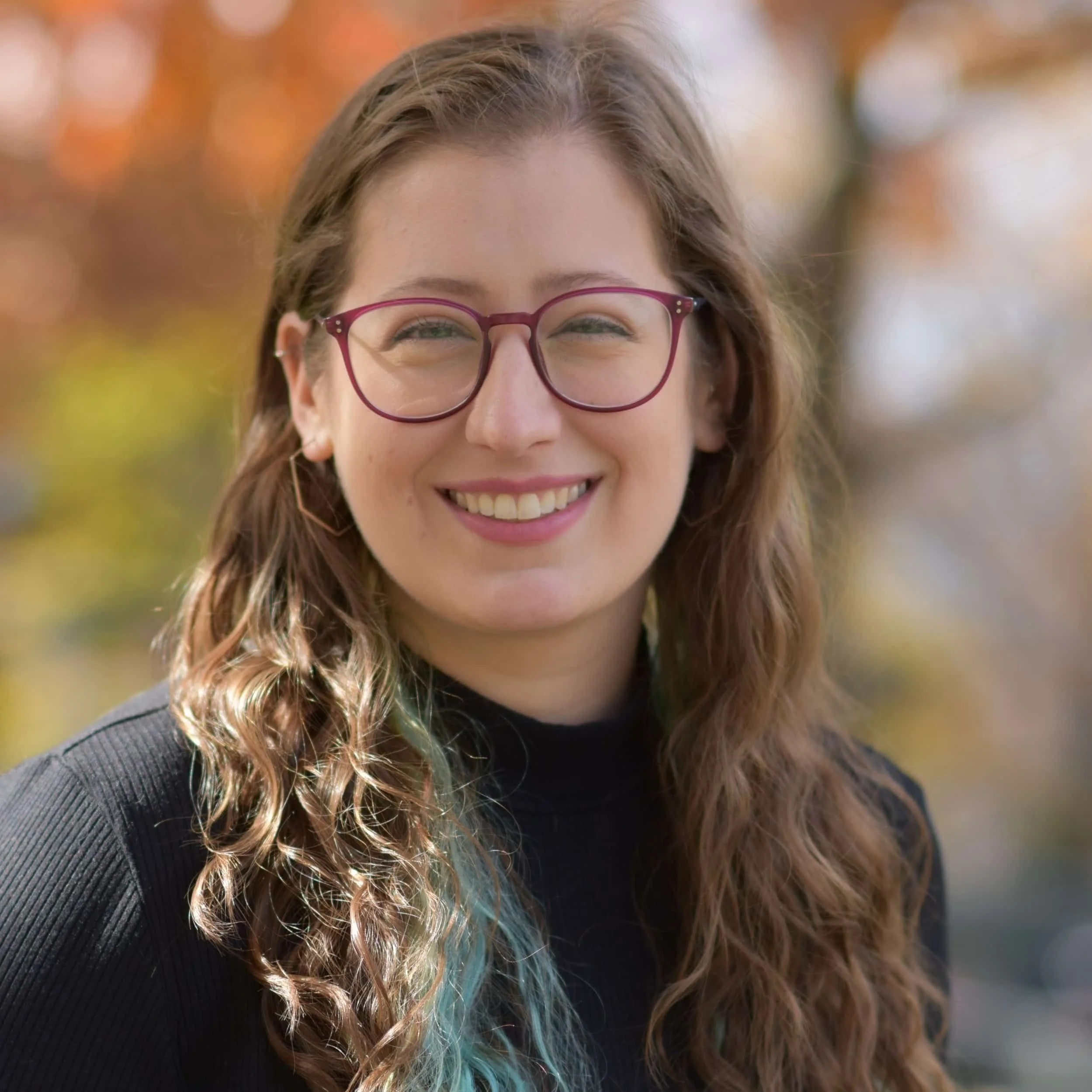 Headshot of Jess Kaufman, wearing purple glasses and a black turtleneck