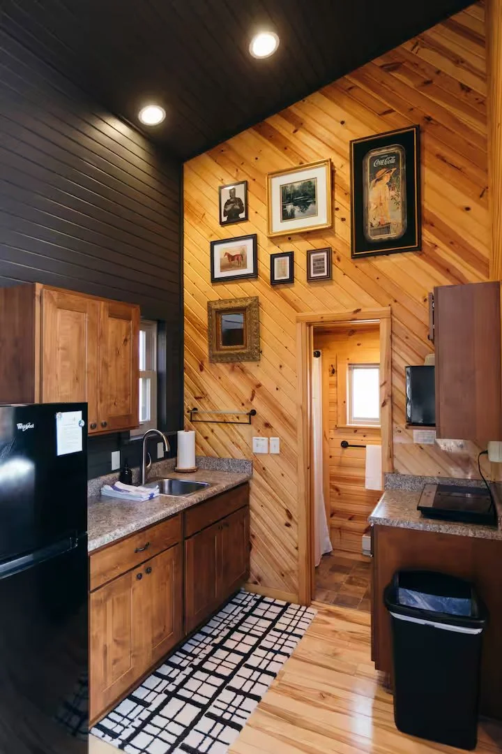 Kitchen with wooden cabinets and paneling, black refrigerator, granite countertops, and a wall decorated with framed artwork and a mirror.