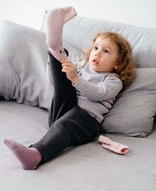 A little girl putting on her socks by herself at home