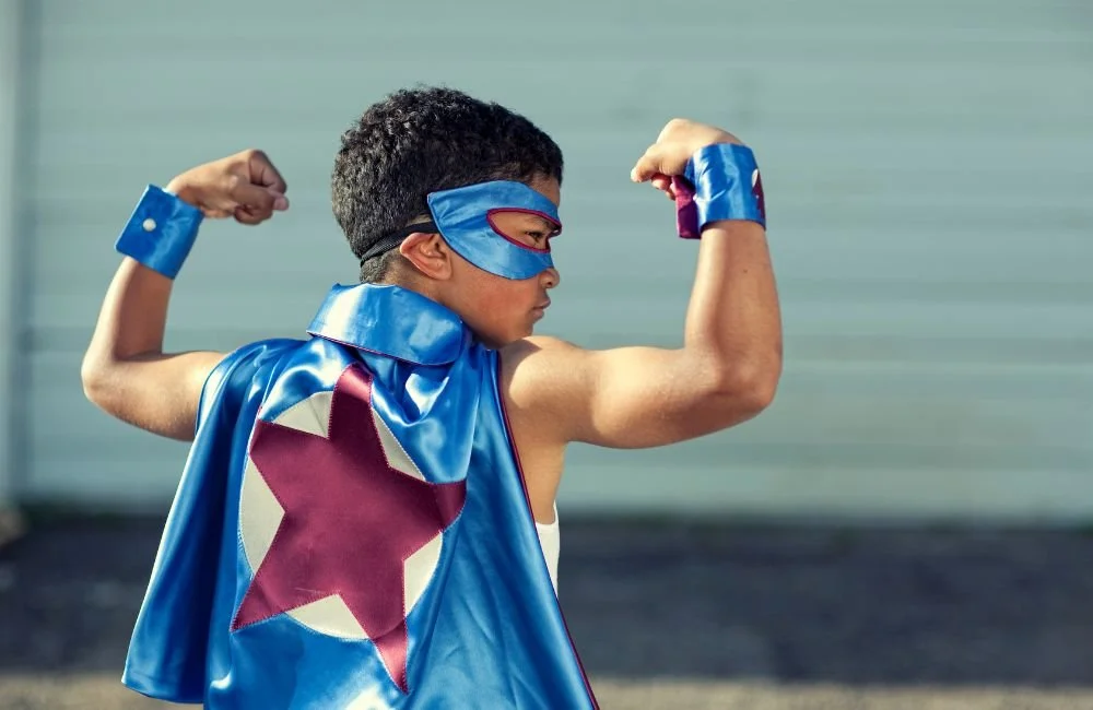 A young boy in a cape flexing his arms in confidence | Orange Seeds Montessori Centre
