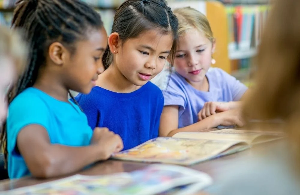 3 little girls reading a picture book in school | Orange Seeds Montessori Centre