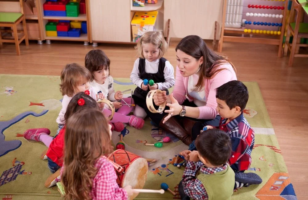 A Montessorian teacher teaching preschoolers musical instrments witting on the ground in a Montessori classroom