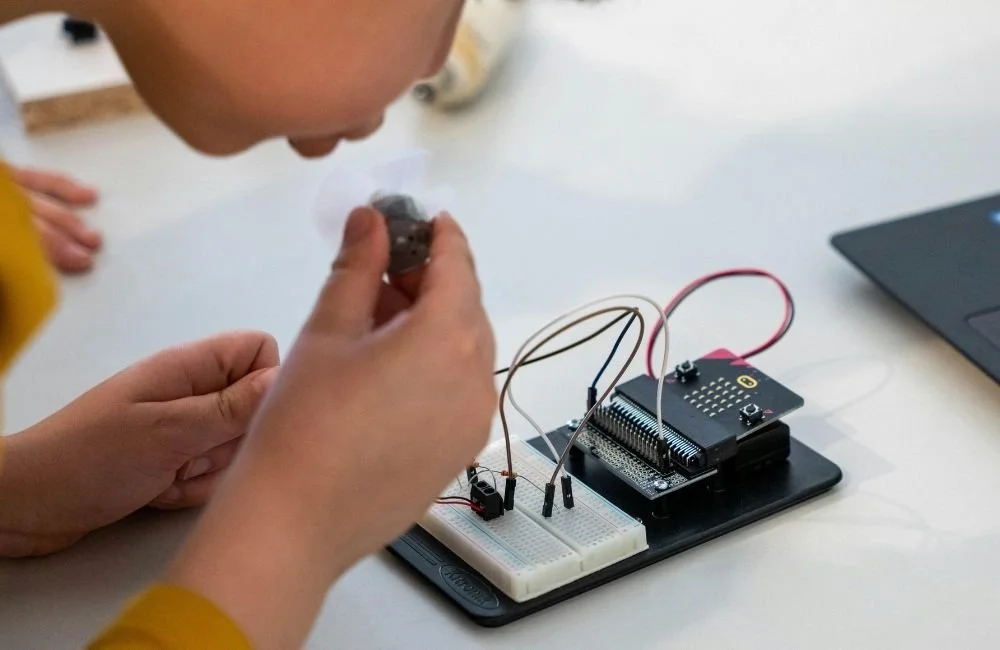 A child looking closely at a device that is wired to activate a mini fan