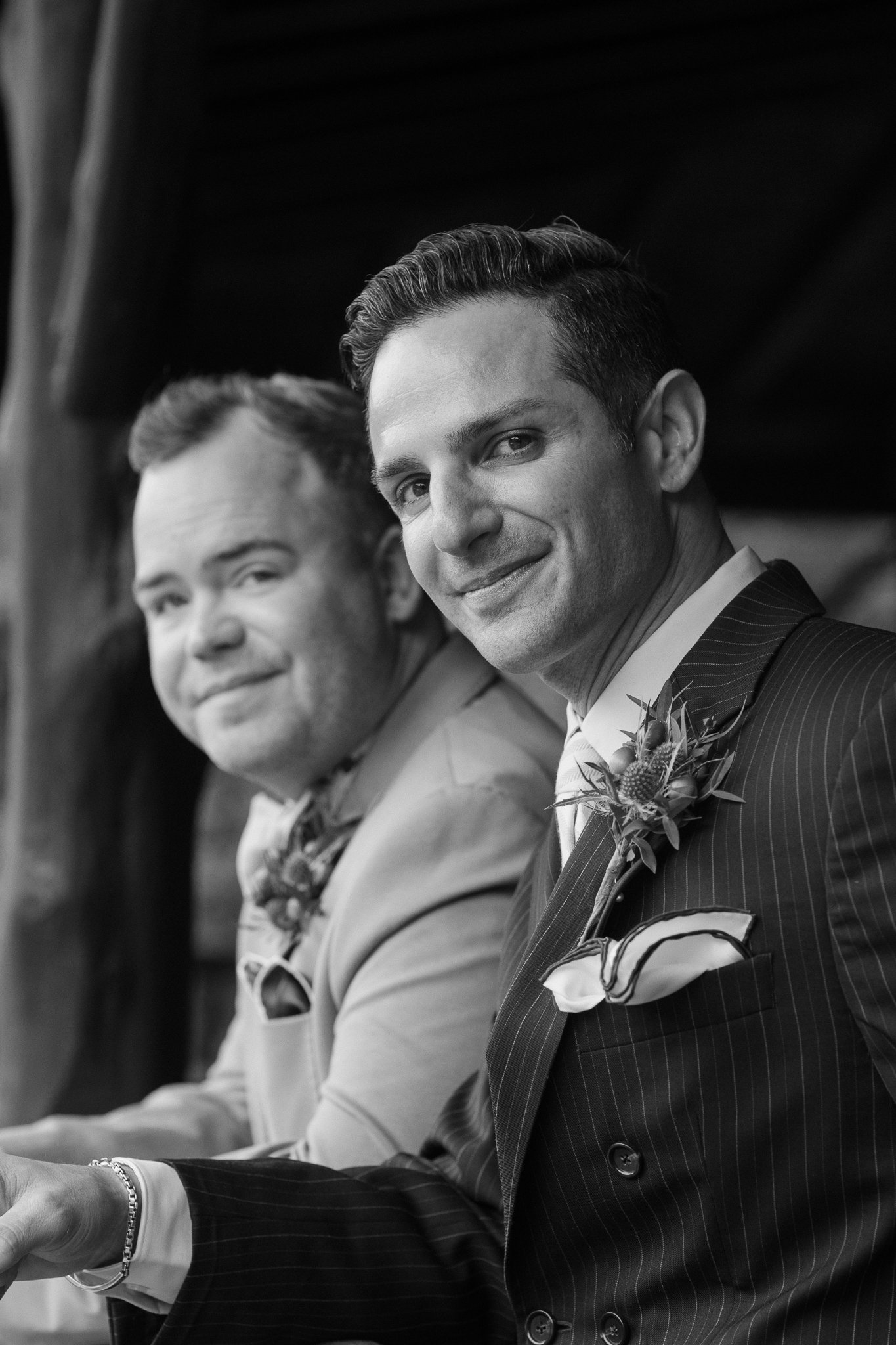 Two men in suits smiling, one wearing a pinstripe suit and boutonniere, black and white photo.