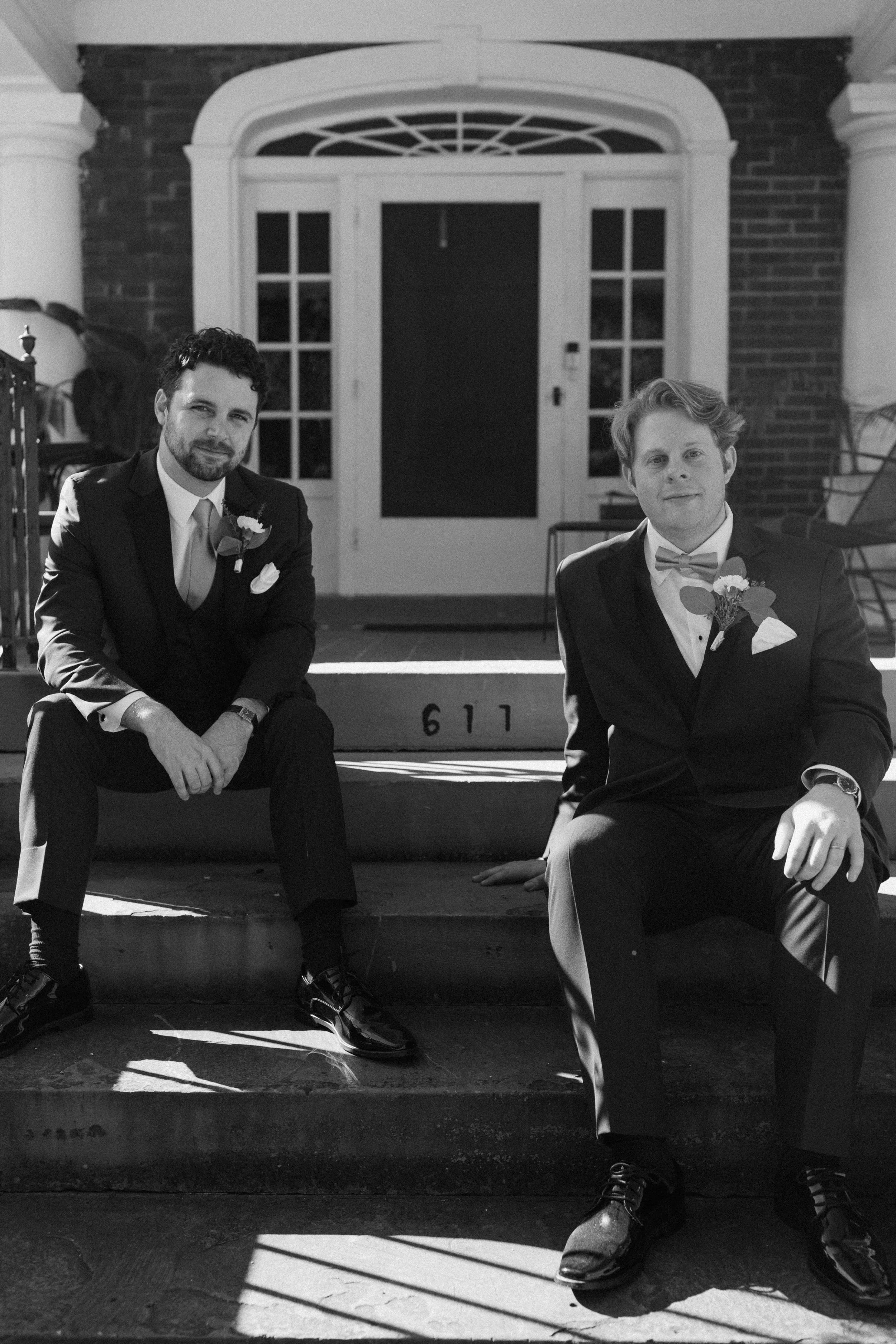 Two men in suits sitting on steps in front of a building entrance, black and white photo.