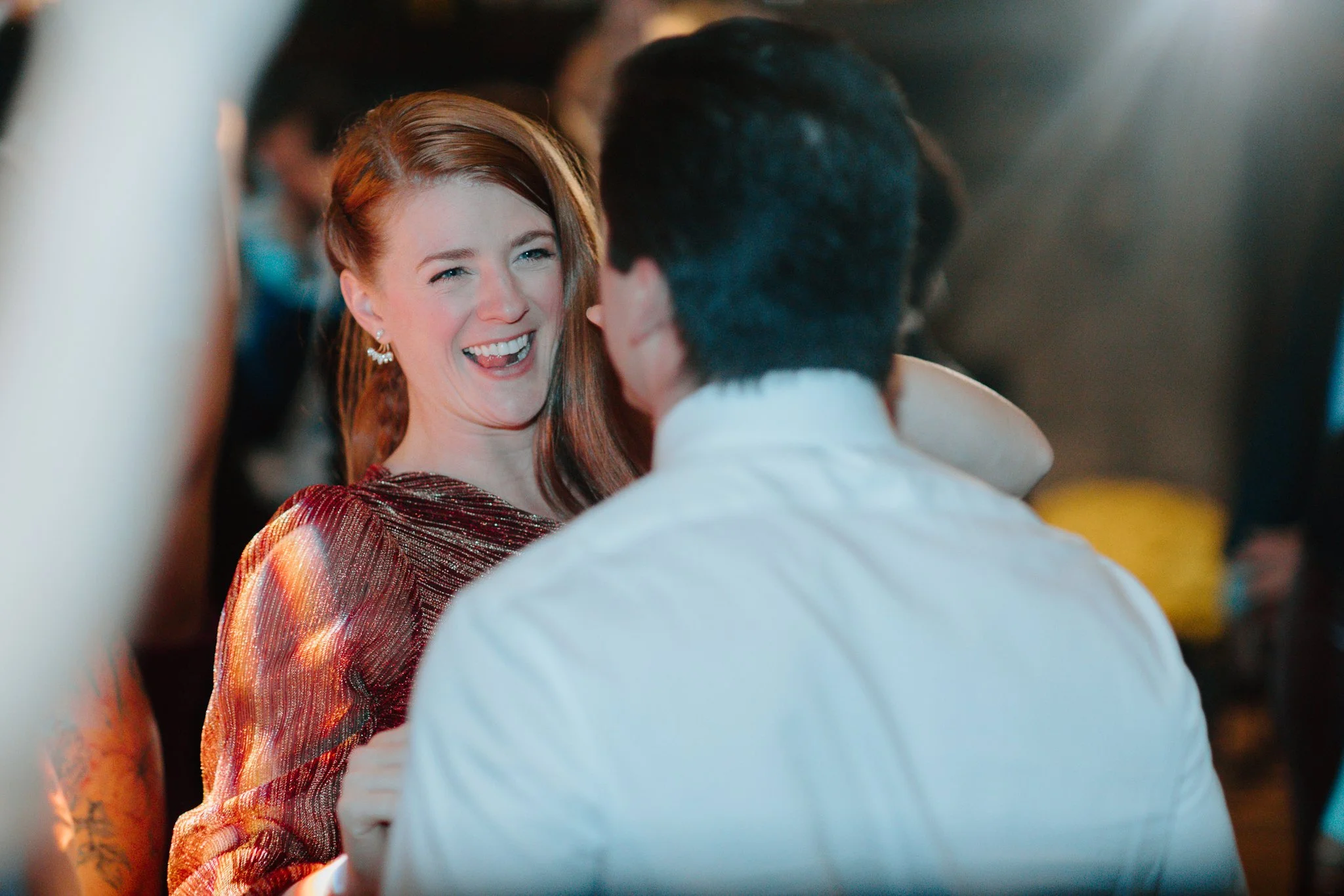 A woman in a red dress smiling and dancing with someone in a white shirt at a lively event.