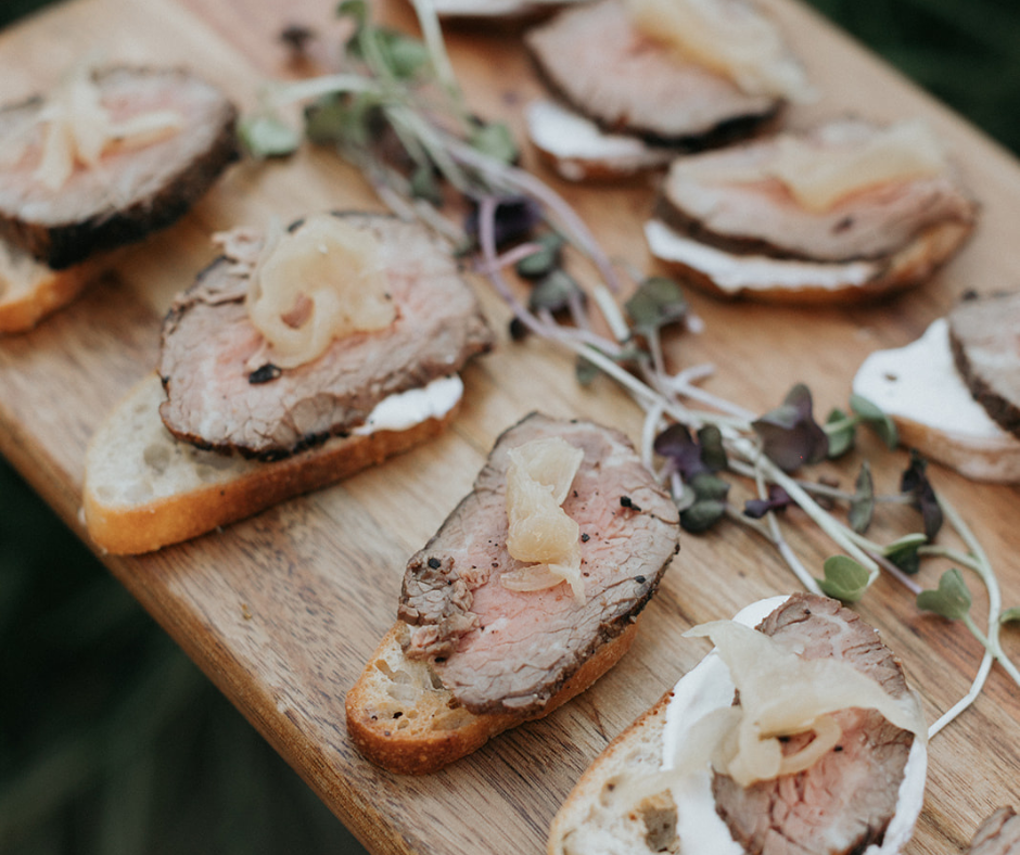 Slices of roast beef topped with cheese or sauce on bread, garnished with microgreens on a wooden serving board.